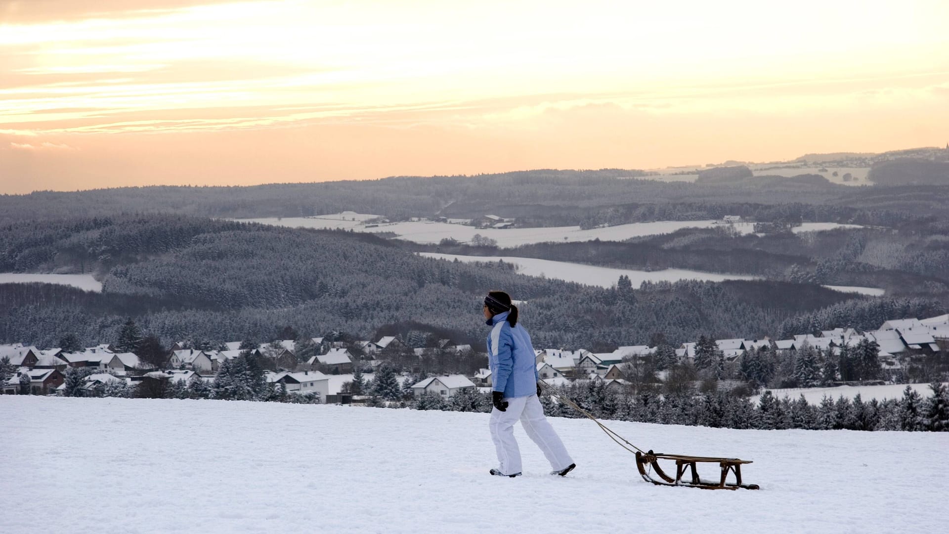 Frau zieht ihren Schlitten durch die Winterlandschaft der Eifel nach Hause (Archivbild).