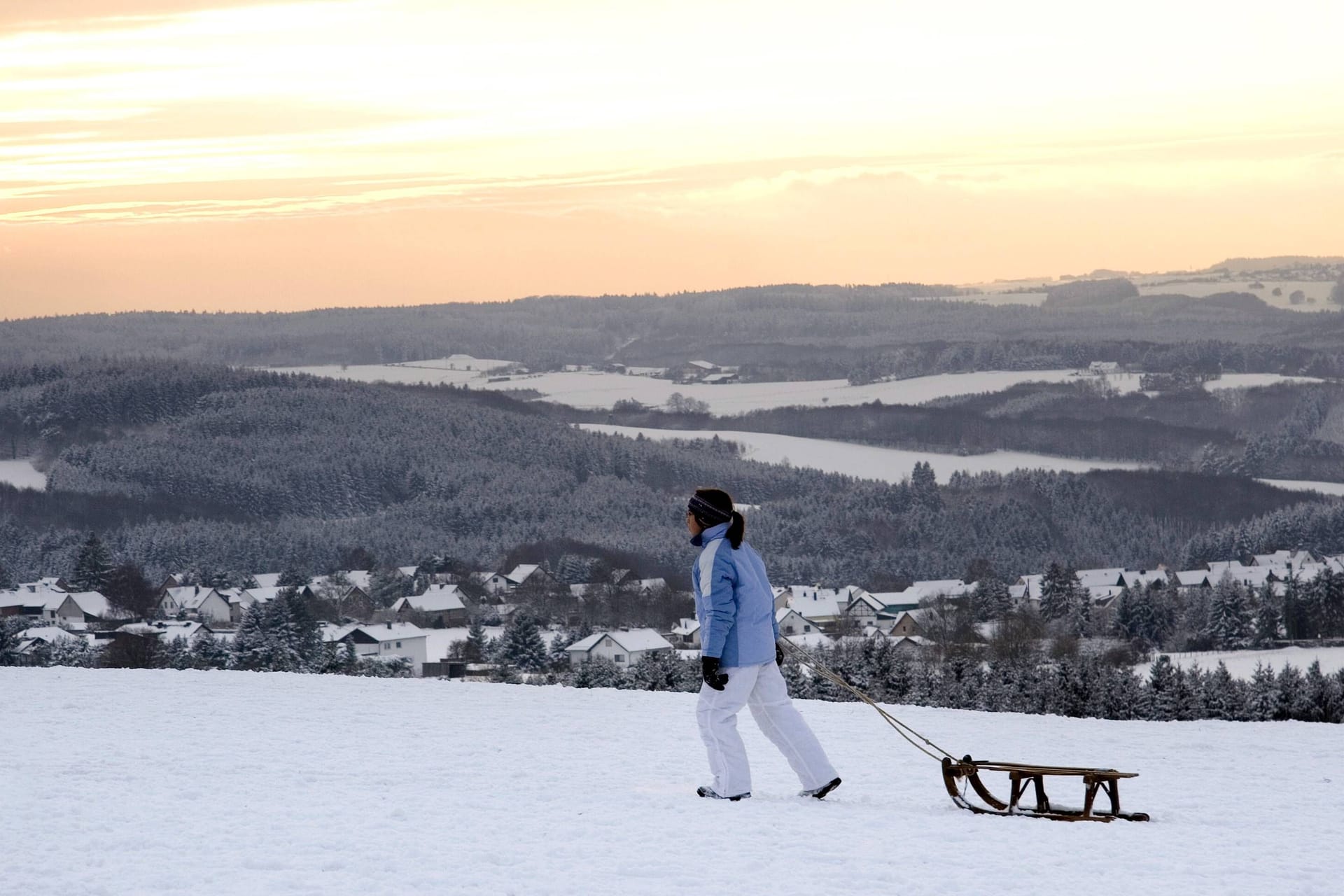 Frau zieht ihren Schlitten durch die Winterlandschaft der Eifel nach Hause (Archivbild).