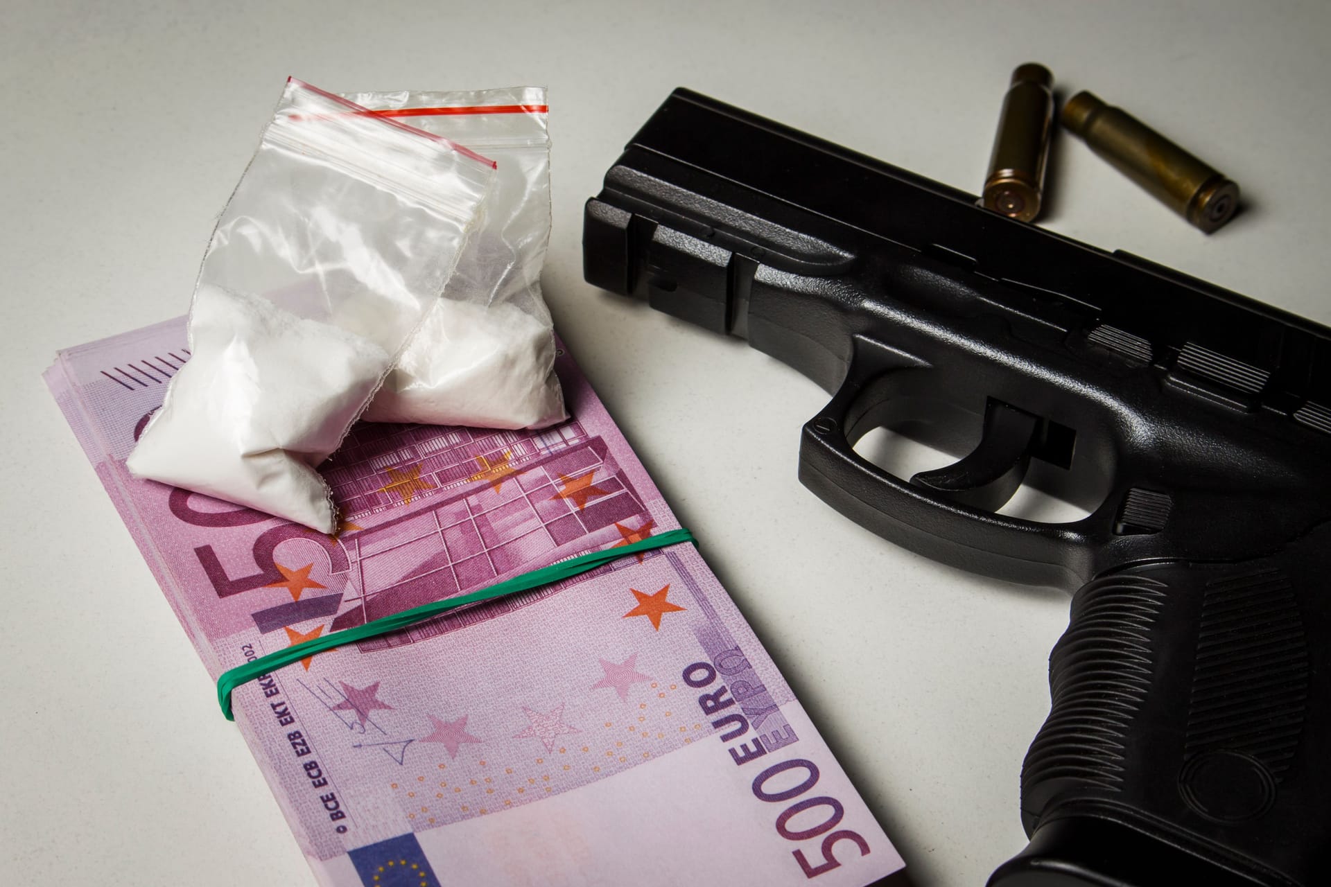 Black gun with a pack of euros and packets of drugs on a white table