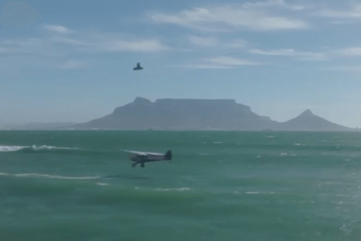 Ein Kitesurfer springt über ein Flugzeug, das ganz nah an der Wasseroberfläche fliegt.