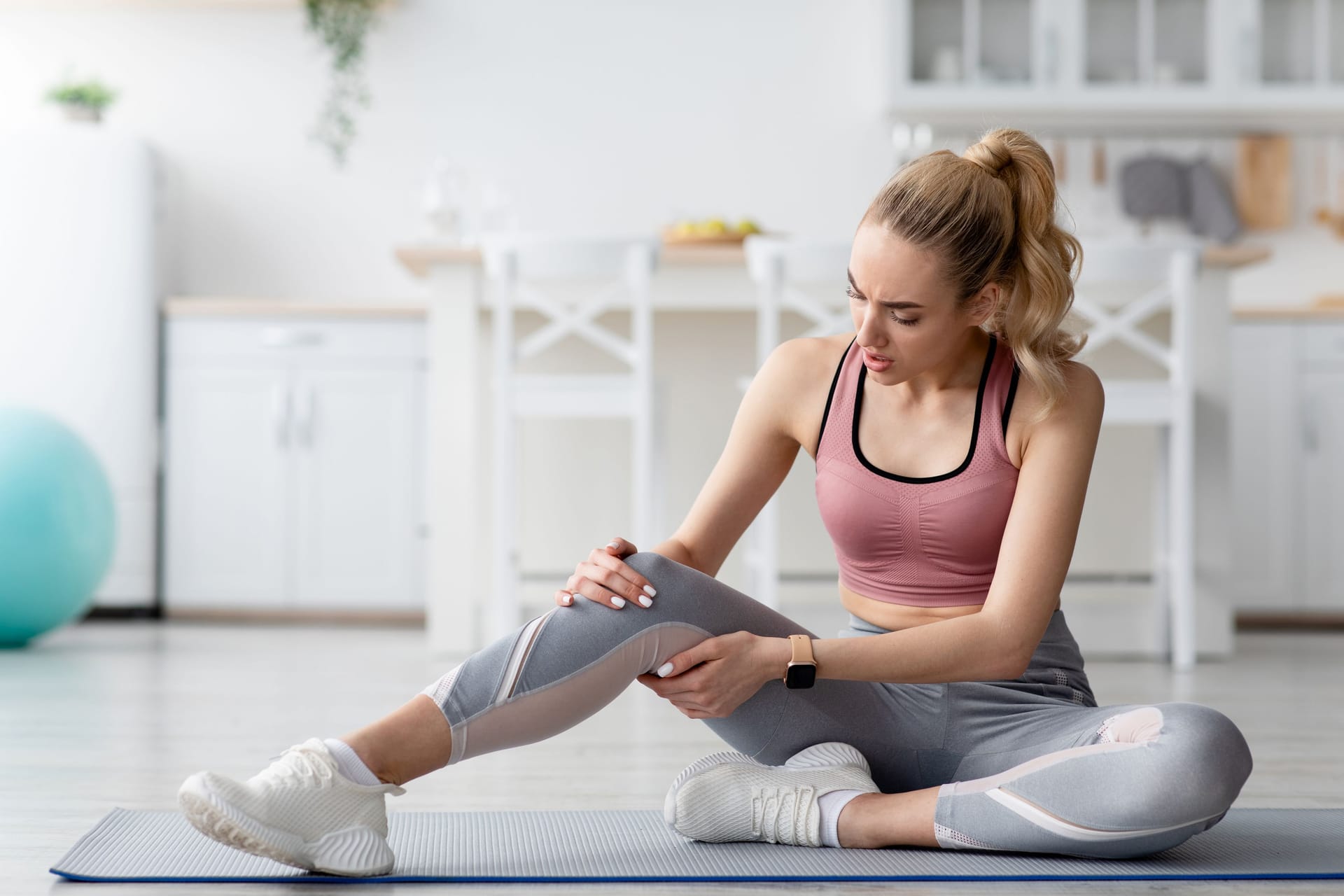 Eine Frau in Sportkleidung sitzt auf einer Yogamatte und hält ihr Bein.