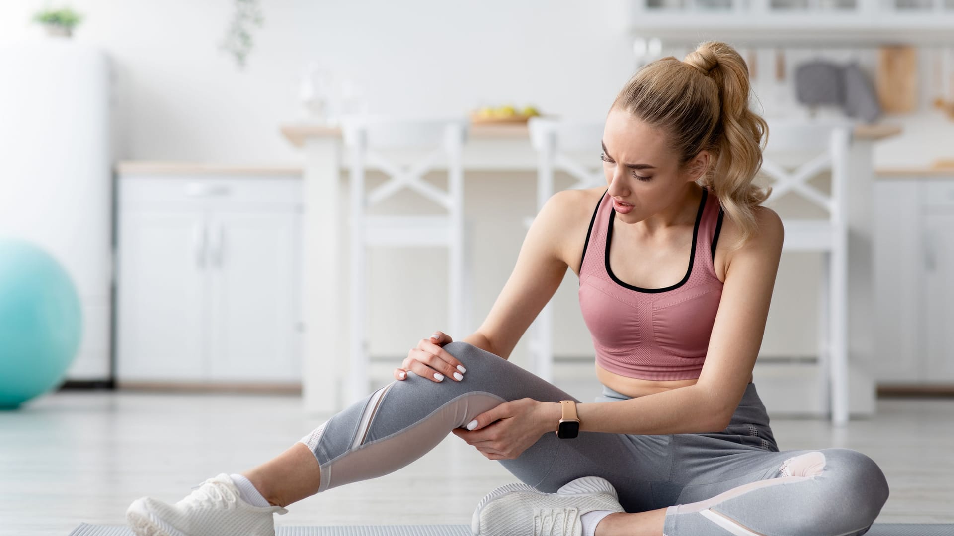 Eine Frau in Sportkleidung sitzt auf einer Yogamatte und hält ihr Bein.