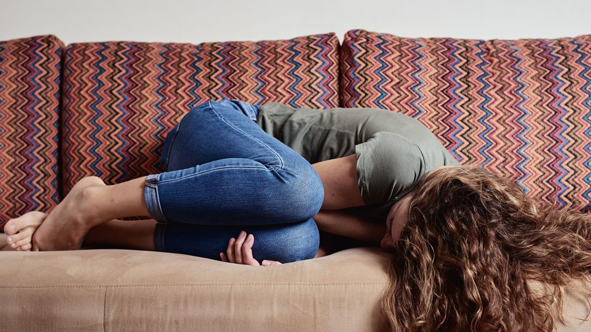 Eine Frau liegt mit Unterleibsschmerzen auf dem Sofa.