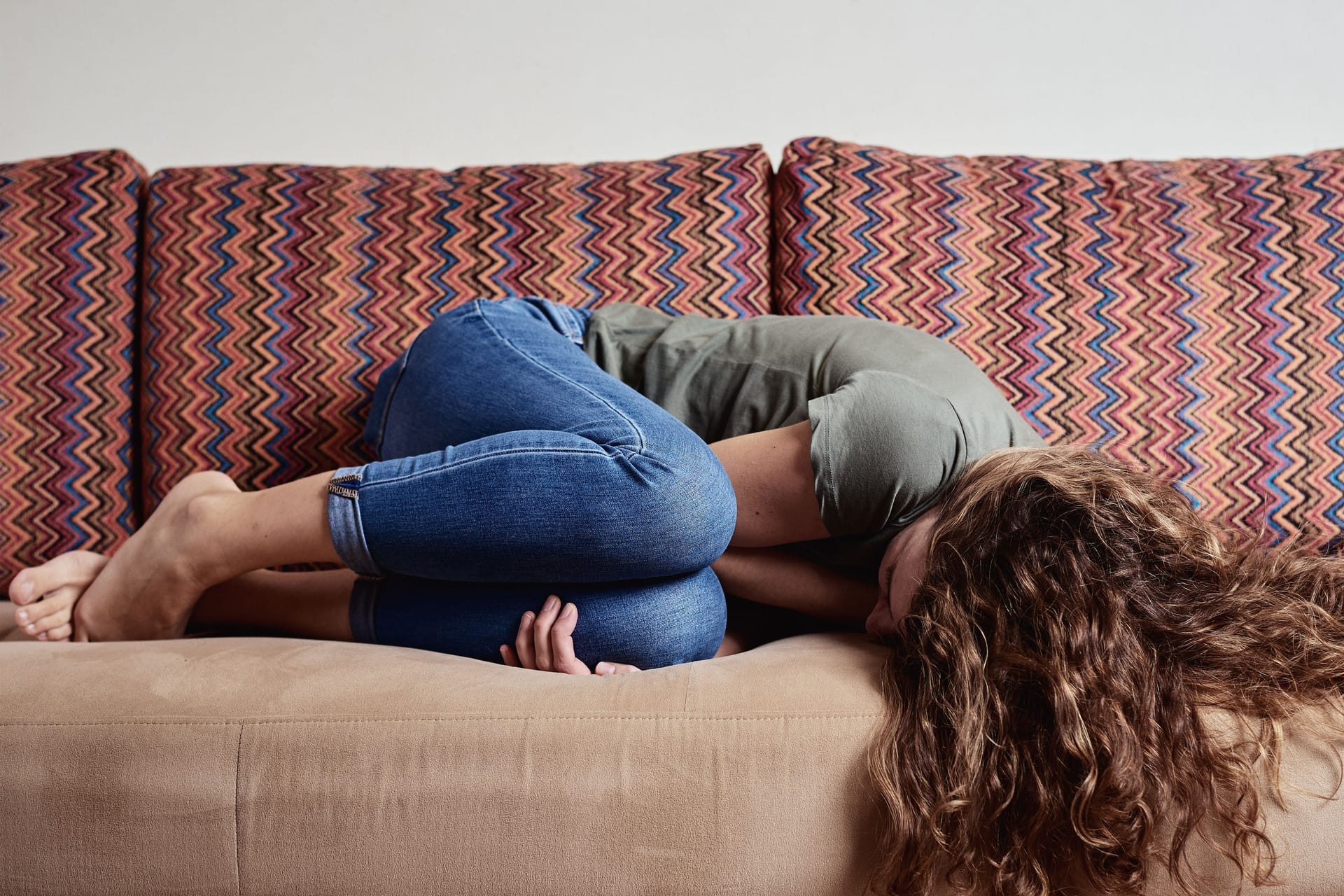 Eine Frau liegt mit Unterleibsschmerzen auf dem Sofa.