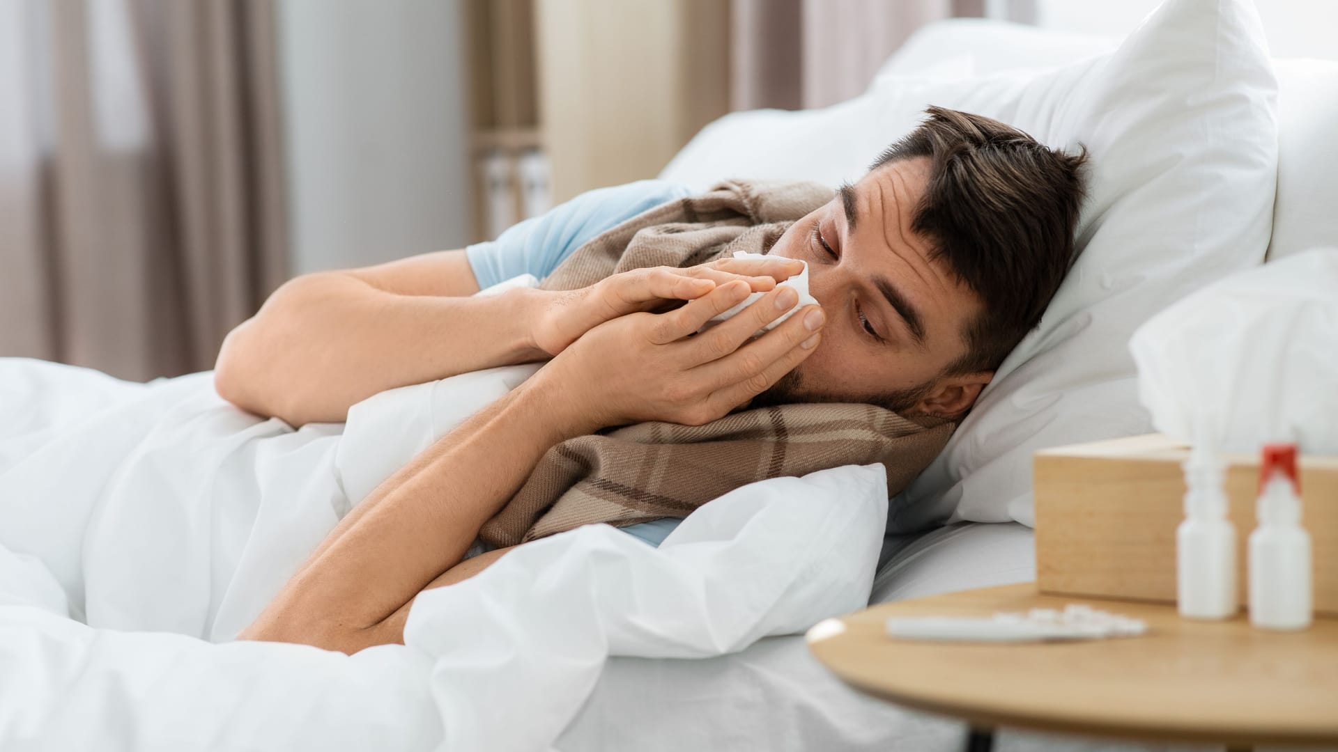 sick man blowing nose lying in bed at home