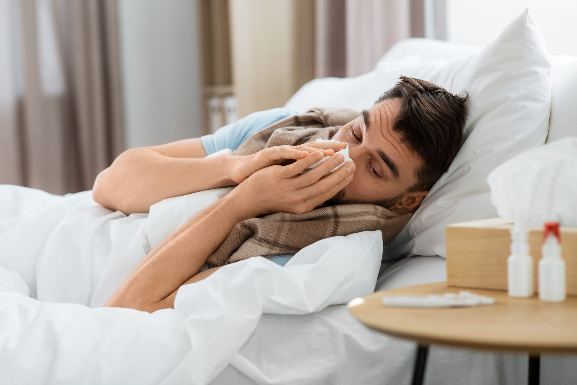 sick man blowing nose lying in bed at home