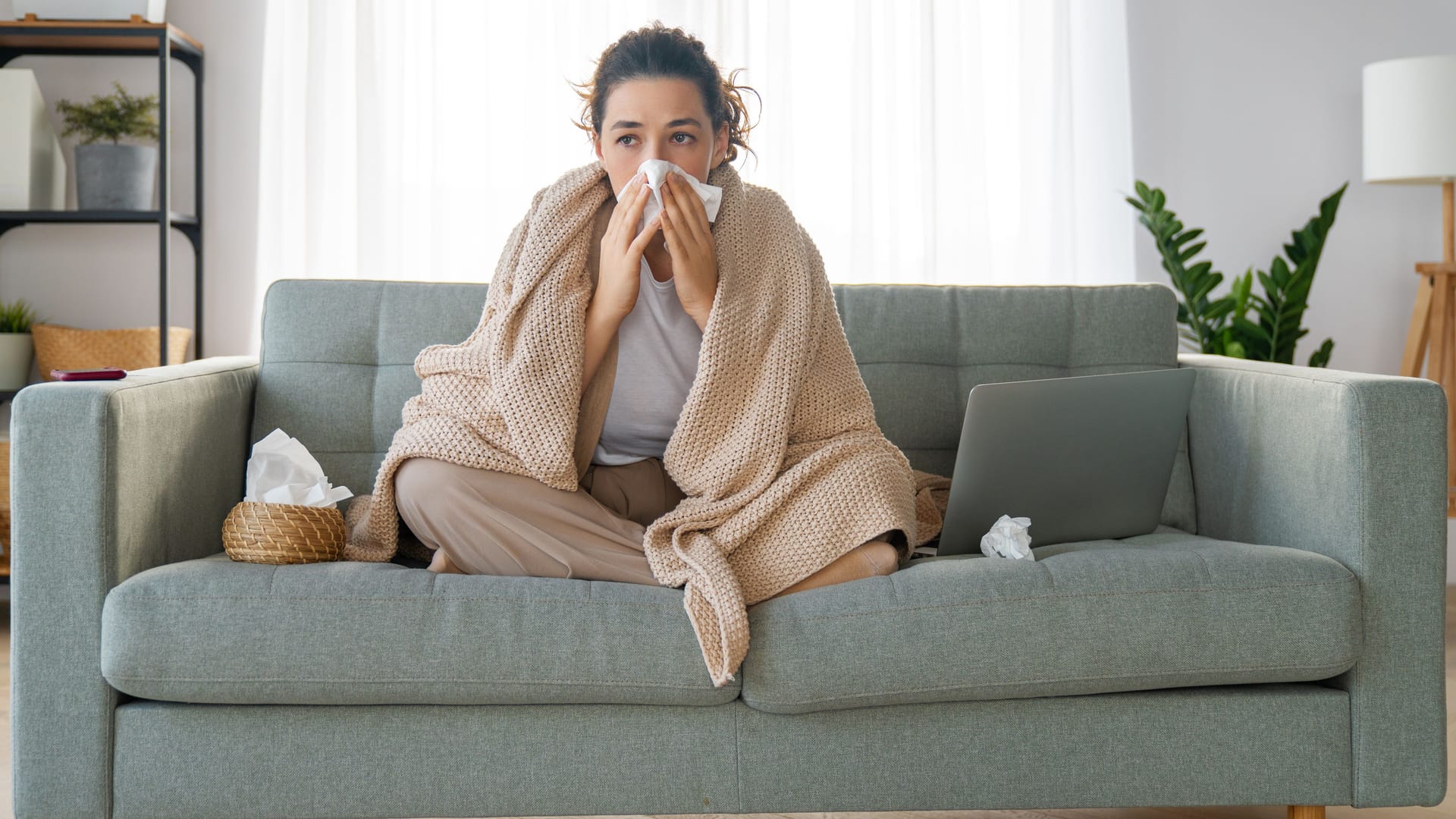 Eine Frau sitzt auf der Couch und putzt sich die Nase.