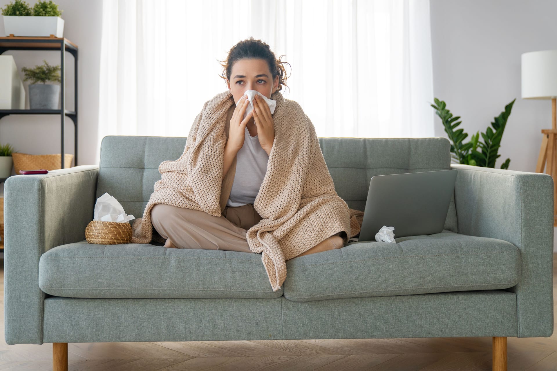 Eine Frau sitzt auf der Couch und putzt sich die Nase.