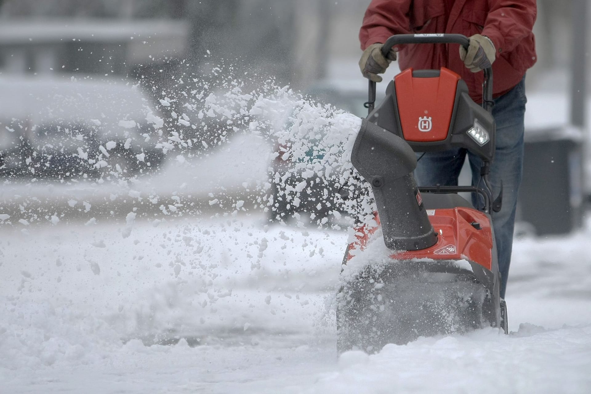 Mann räumt mit Hilfe einer Schneefräse den Gehweg