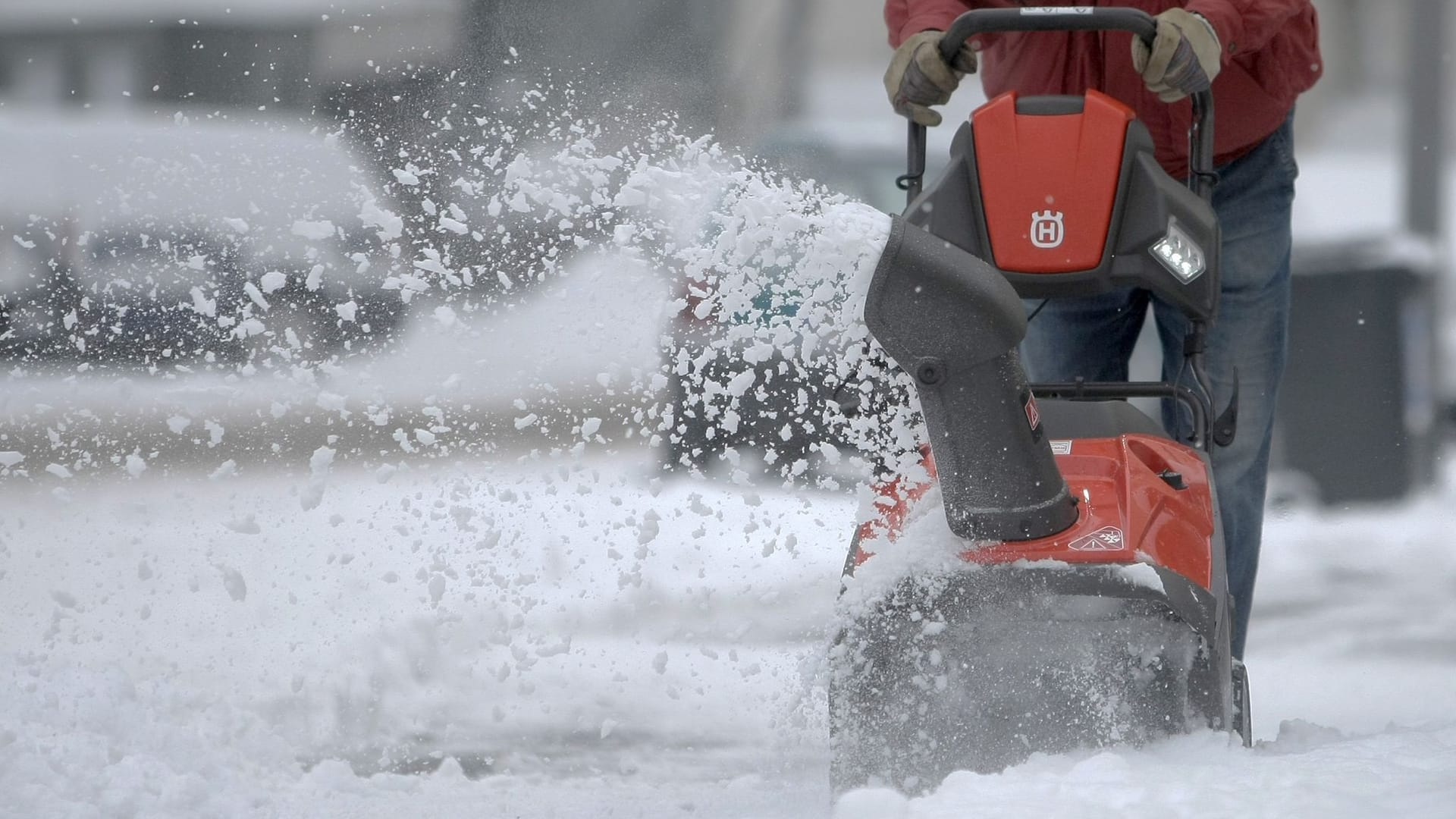 Mann räumt mit Hilfe einer Schneefräse den Gehweg