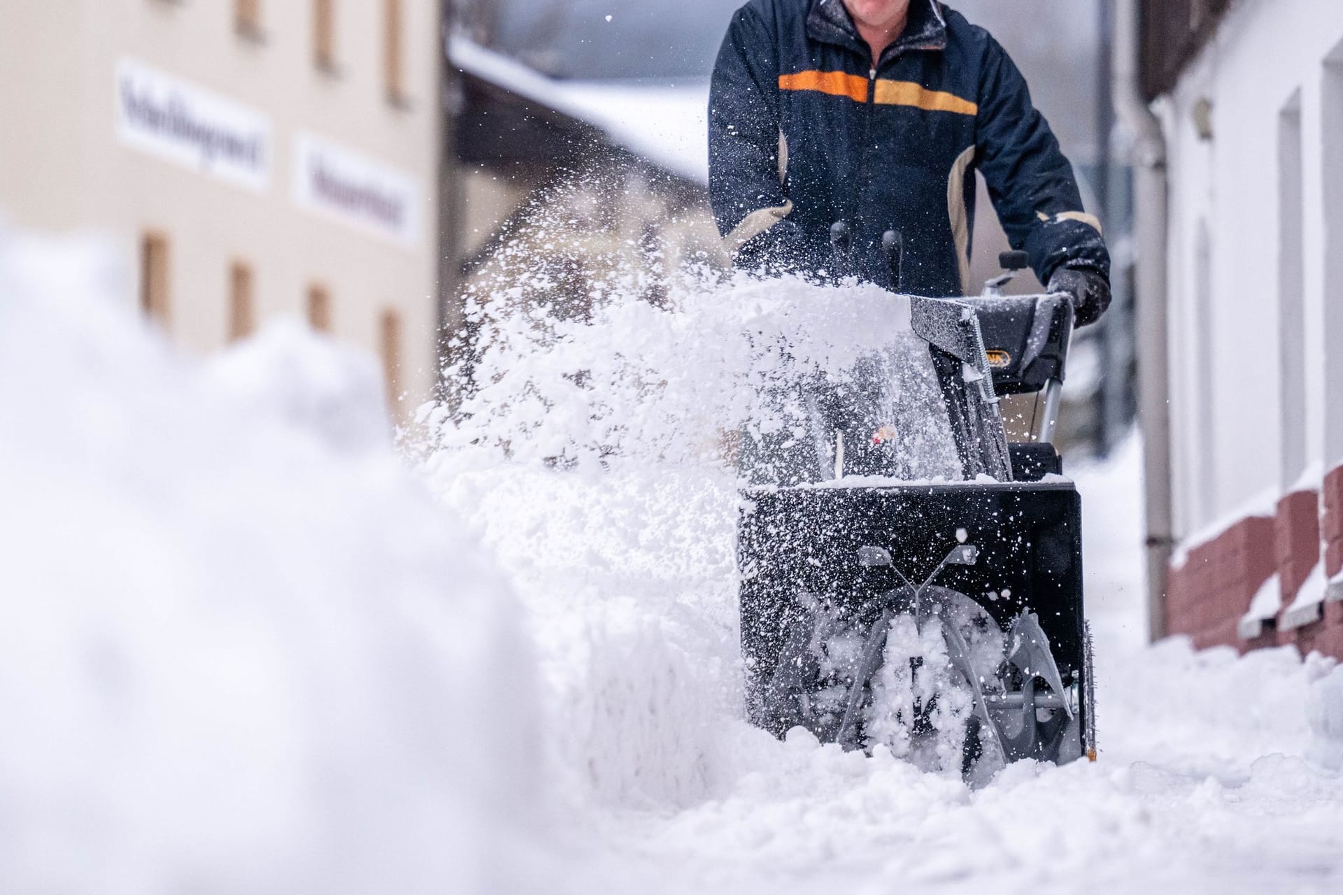 Ein Mann beräumt den Gehweg mit einer Schneefräse