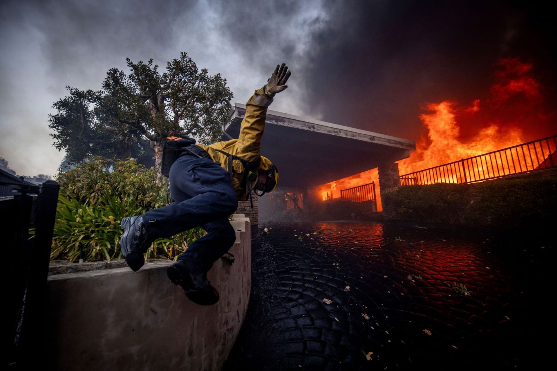 Ein Feuerwehrmann springt über einen Zaun, während er das Palisades-Feuer im Stadtteil Pacific Palisades bekämpft.