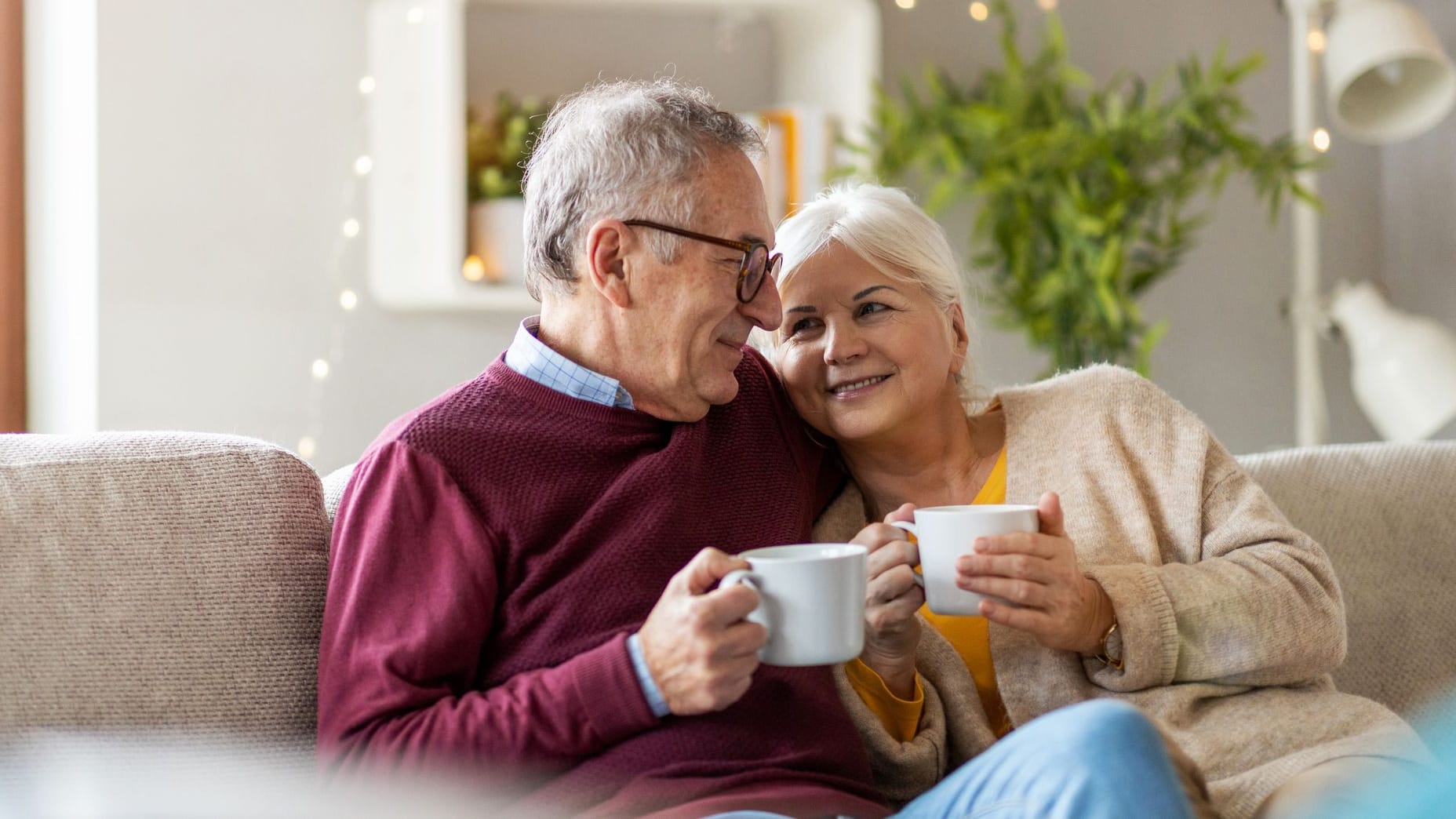 Rentnerpaar sitzt zu Hause auf dem Sofa und trinkt Kaffee