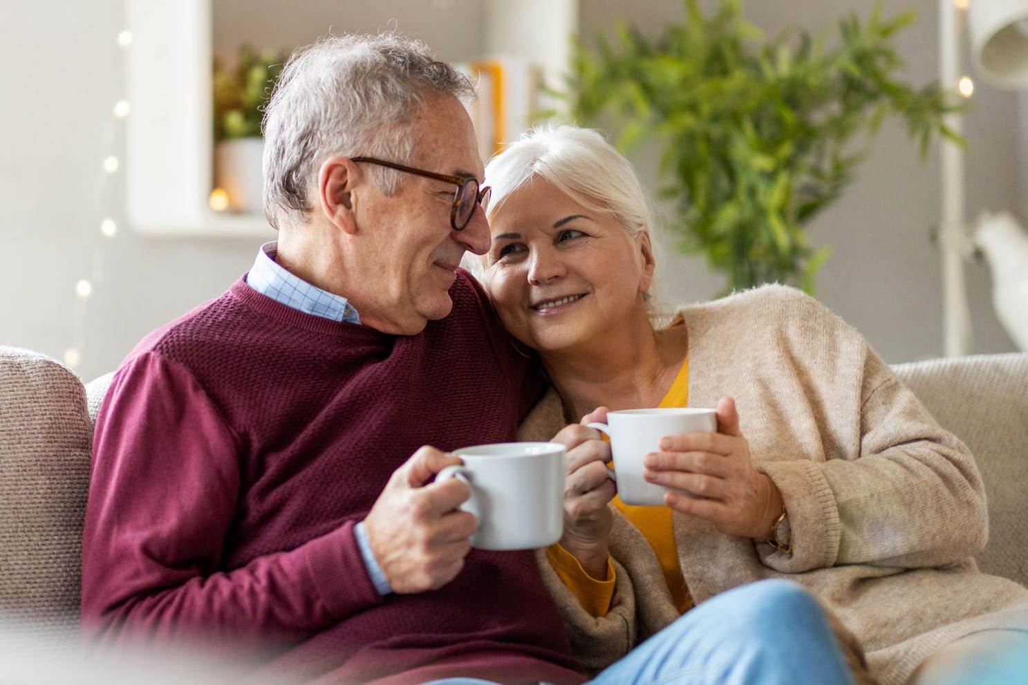 Rentnerpaar sitzt zu Hause auf dem Sofa und trinkt Kaffee