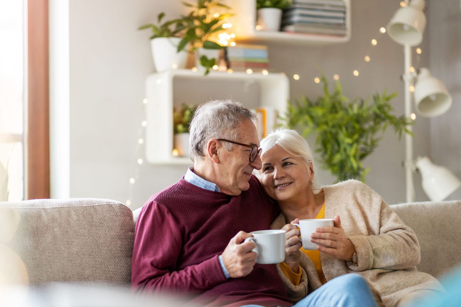 Rentnerpaar sitzt zu Hause auf dem Sofa und trinkt Kaffee