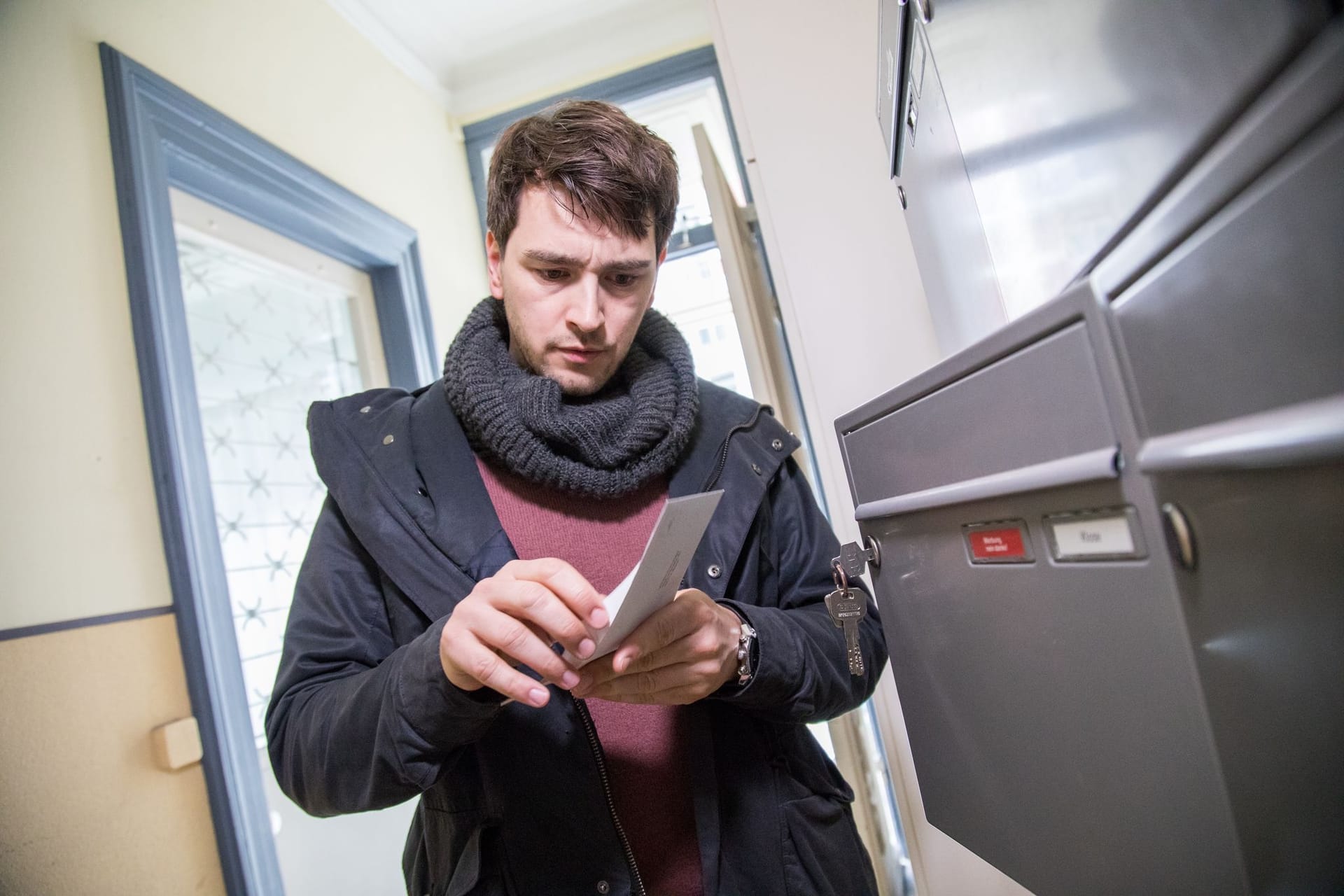 Mann öffnet Brief an einem Briefkasten im Hausflur