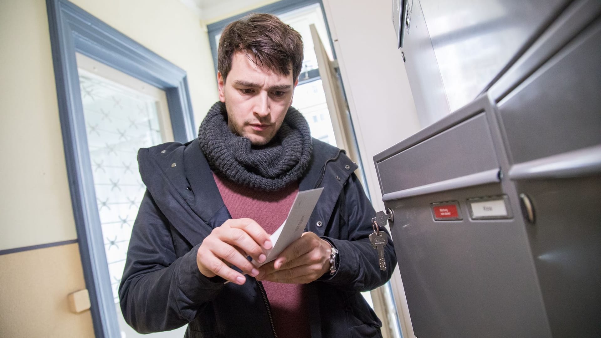 Mann öffnet Brief an einem Briefkasten im Hausflur