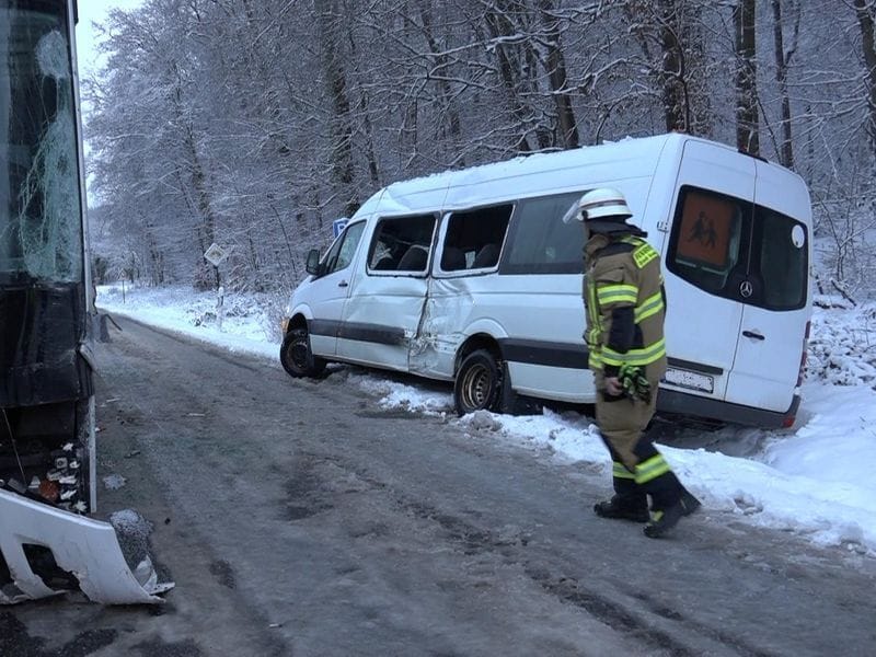 Ein Feuerwehrmann steht nach einem Unfall zwischen einem Linien- und einem kleinen Schulbus an der Einsatzstelle auf einer schneeglatten Landstraße.