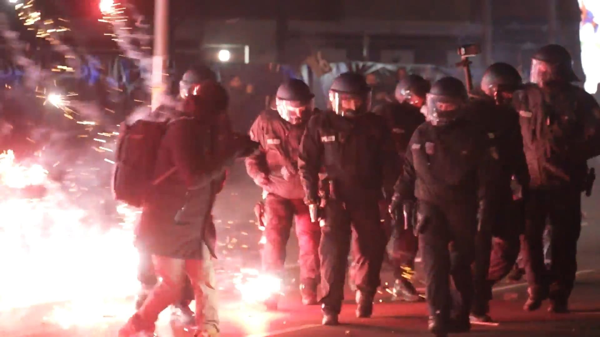 ARCHIV - 01.01.2025, Berlin: Einsatzkräfte der Polizei stehen in der Silvesternacht zwischen brennendem Feuerwerk in Neukölln.