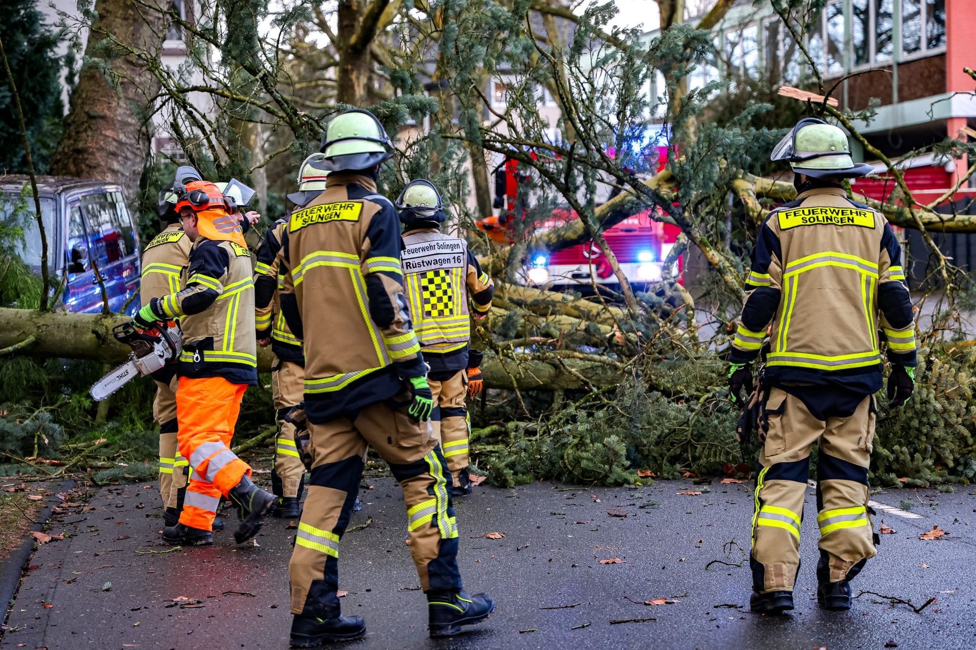 Einsatzkräfte der Feuerwehr stehen vor einem umgestürzten Baum in Solingen und zerkleinern diesen mit Kettensägen: Landesweit sorgt der Sturm für zahlreiche Einsätze der Feuerwehr.