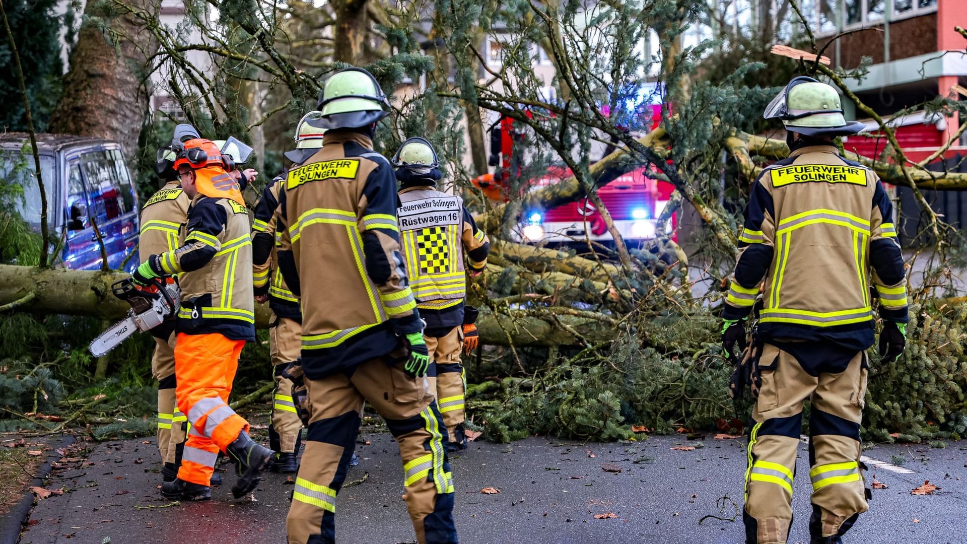 Einsatzkräfte der Feuerwehr stehen vor einem umgestürzten Baum in Solingen und zerkleinern diesen mit Kettensägen: Landesweit sorgt der Sturm für zahlreiche Einsätze der Feuerwehr.