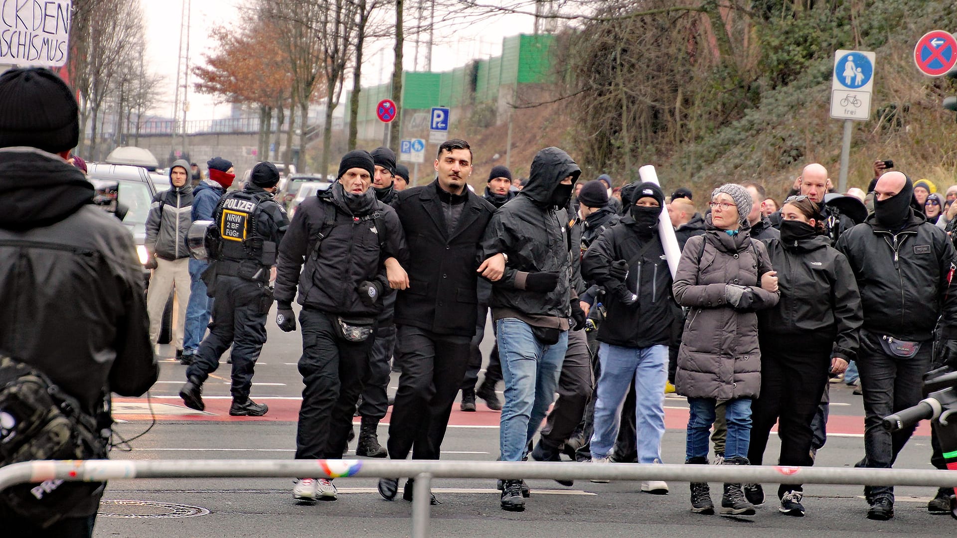 Arm in Arm eingehakt: Ex-AfD-Politiker Ferhat Sentürk (mittig, schwarzer Mantel) läuft zusammen mit Teilnehmern der Demo sowie der AfD-Funktionärin Gisela Ellgoth (rechts im Bild, grauer Mantel) durch Aachen.