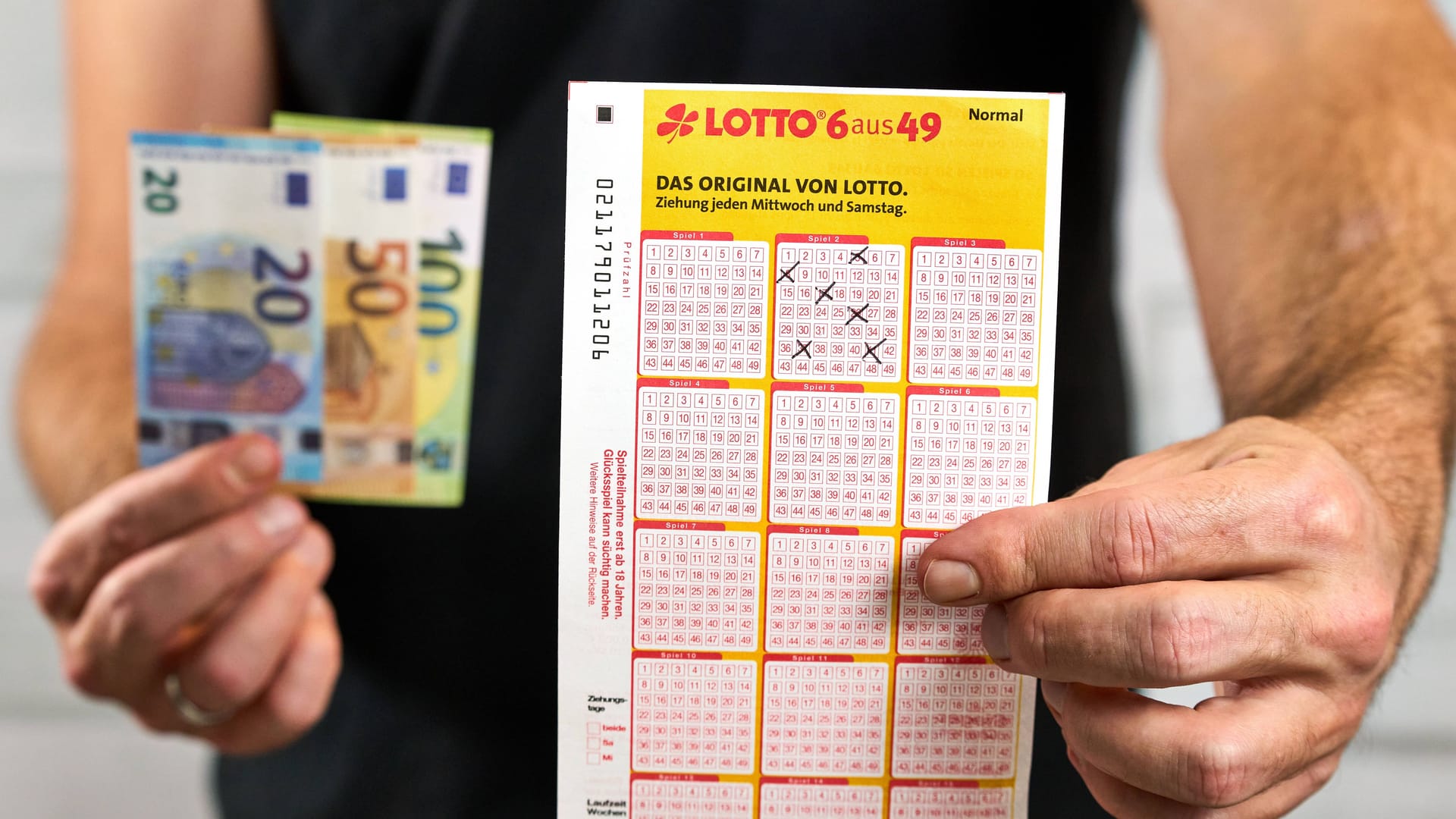 Mann mit Geld- und Lottospielscheinen. (Symbolfoto)