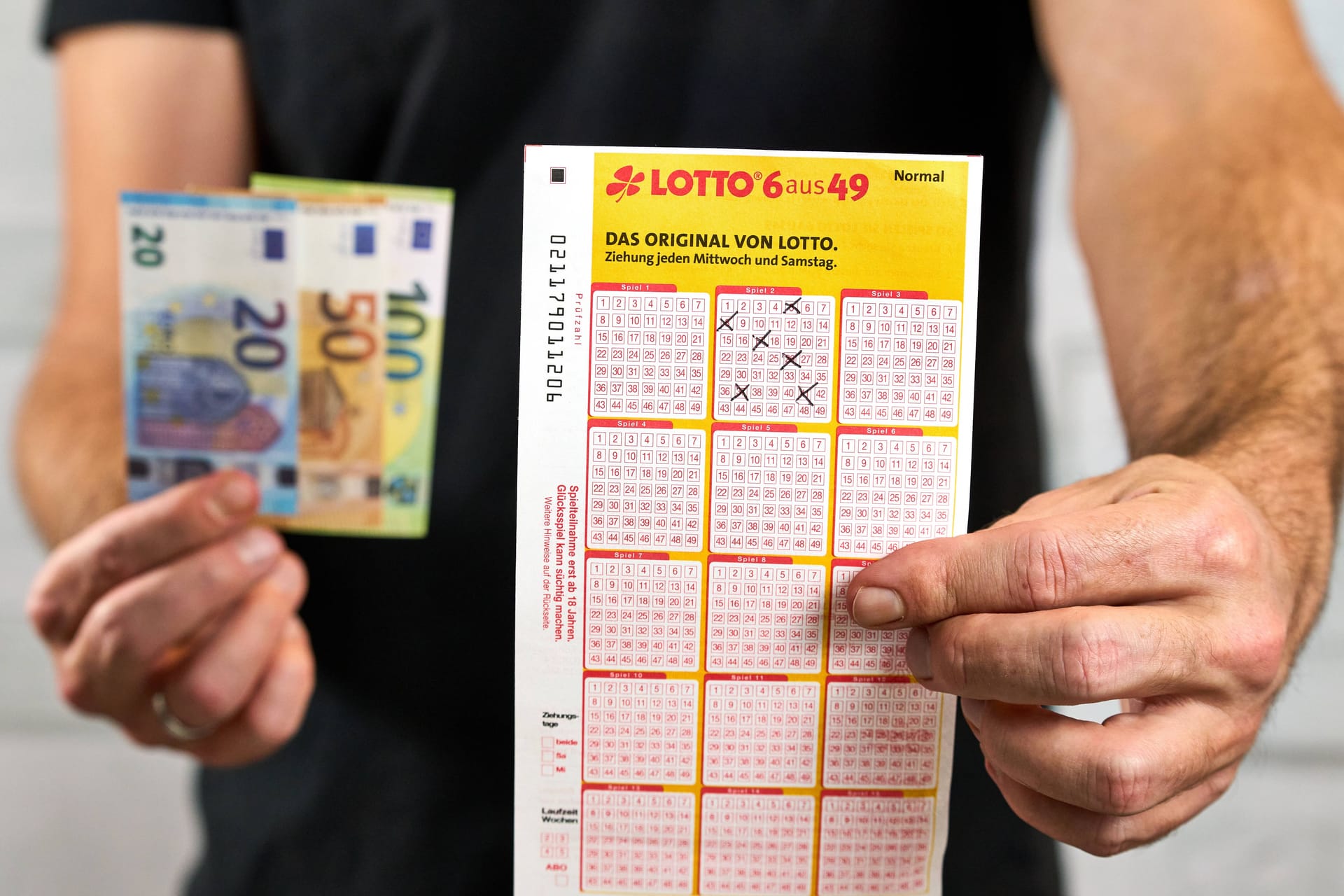 Mann mit Geld- und Lottospielscheinen. (Symbolfoto)