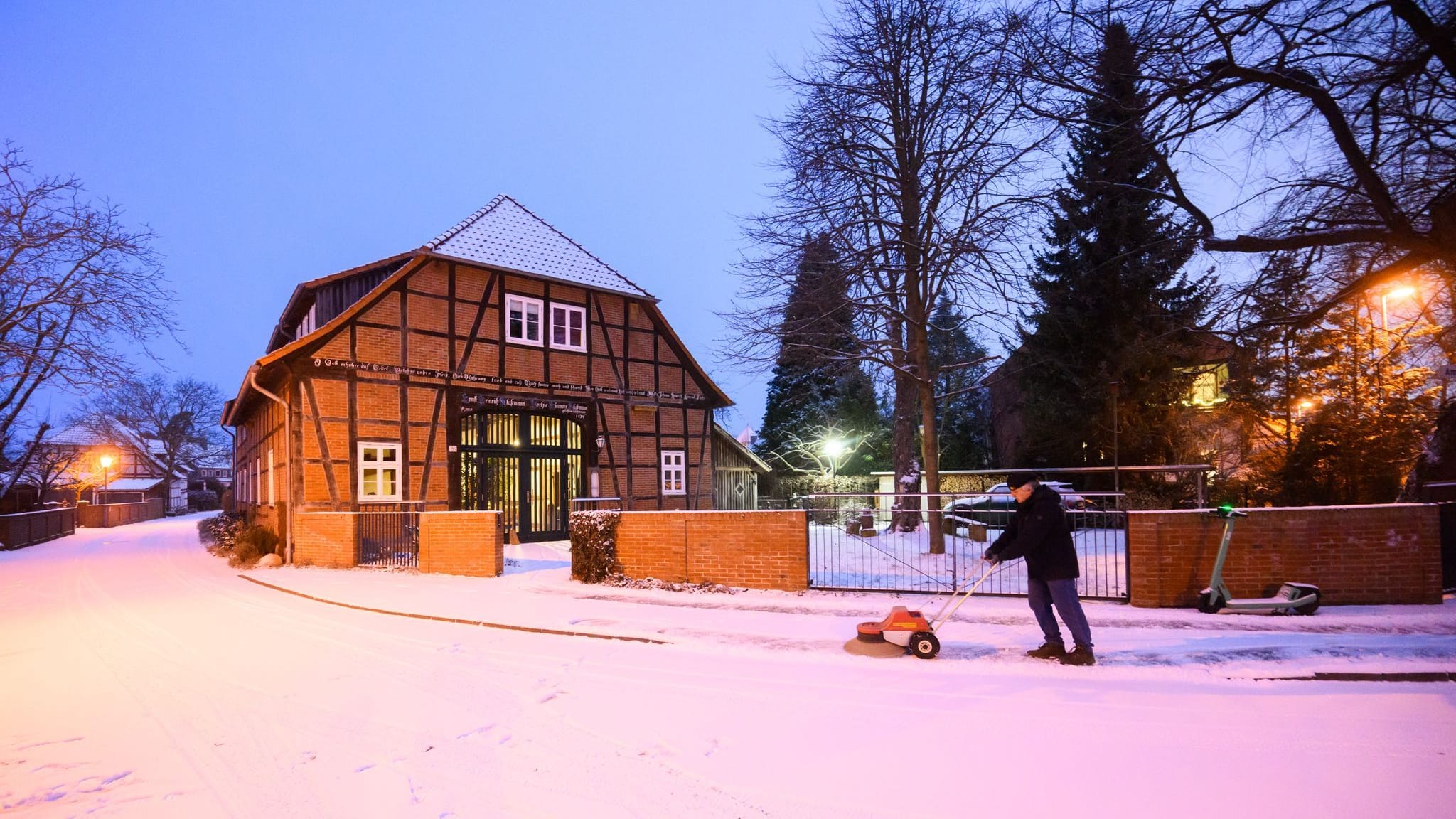 Wetter: Ein Mann fegt mit einer Maschine Schnee vor einem Fachwerkhaus in der Region Hannover. In Deutschland bringt die kalte Polarluft Schnee mit sich.