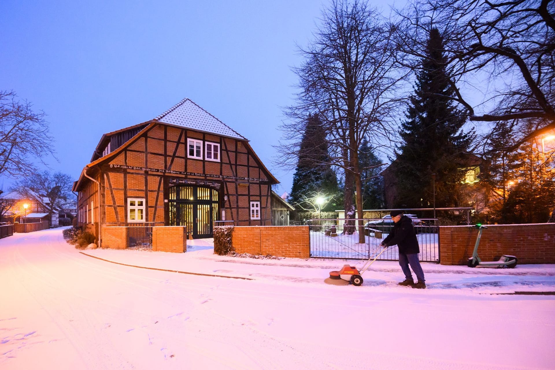 Wetter: Ein Mann fegt mit einer Maschine Schnee vor einem Fachwerkhaus in der Region Hannover. In Deutschland bringt die kalte Polarluft Schnee mit sich.