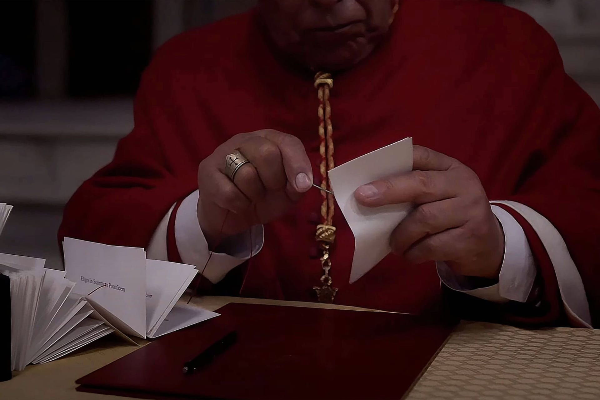 Eine Szene aus dem Film "Konklave": Ein Wahlhelfer durchsticht die abgegebenen Wahlzettel mit einer Nadel und reiht sie auf eine Schnur. So wird sichergestellt, dass bei der Papstwahl keine Stimme verloren geht.