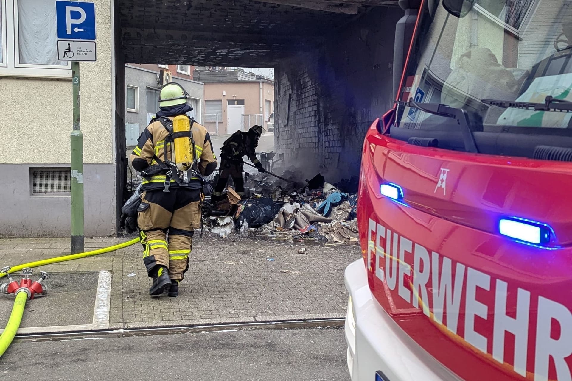 Die Feuerwehr beseitigt brennenden Sperrmüll in einer Einfahrt: In Essen ist dadurch ein massiver Gebäudeschaden entstanden. Die Polizei geht von Brandstiftung aus.