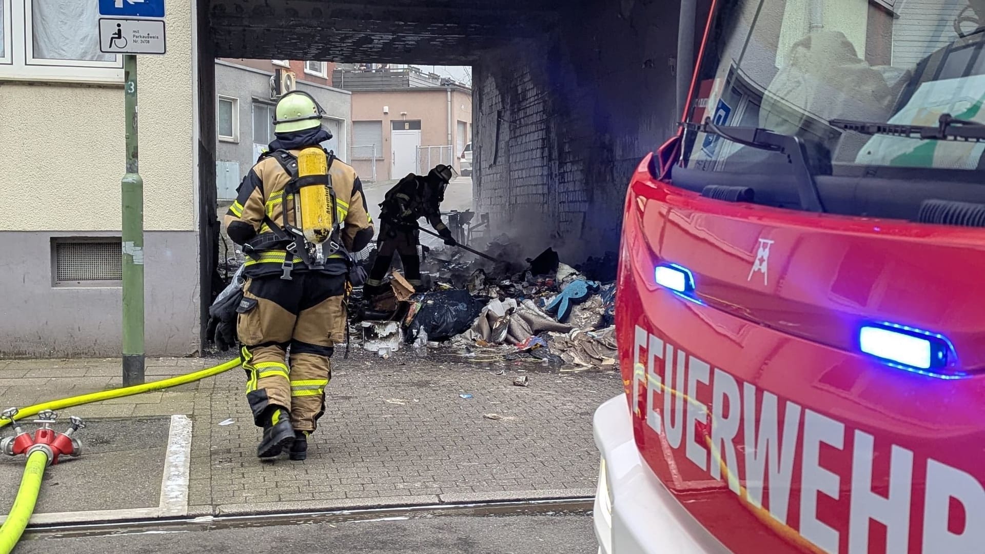 Die Feuerwehr beseitigt brennenden Sperrmüll in einer Einfahrt: In Essen ist dadurch ein massiver Gebäudeschaden entstanden. Die Polizei geht von Brandstiftung aus.