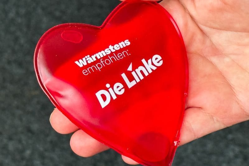 Ein Frau hält im Rahmen eines Pressetermins zur Landesvertreterversammlung der Linken Sachsen zur Bundestagswahl einen Handwärmer mit der Aufschrift „Wärmstens empfohlen Die Linke“ in der Hand.