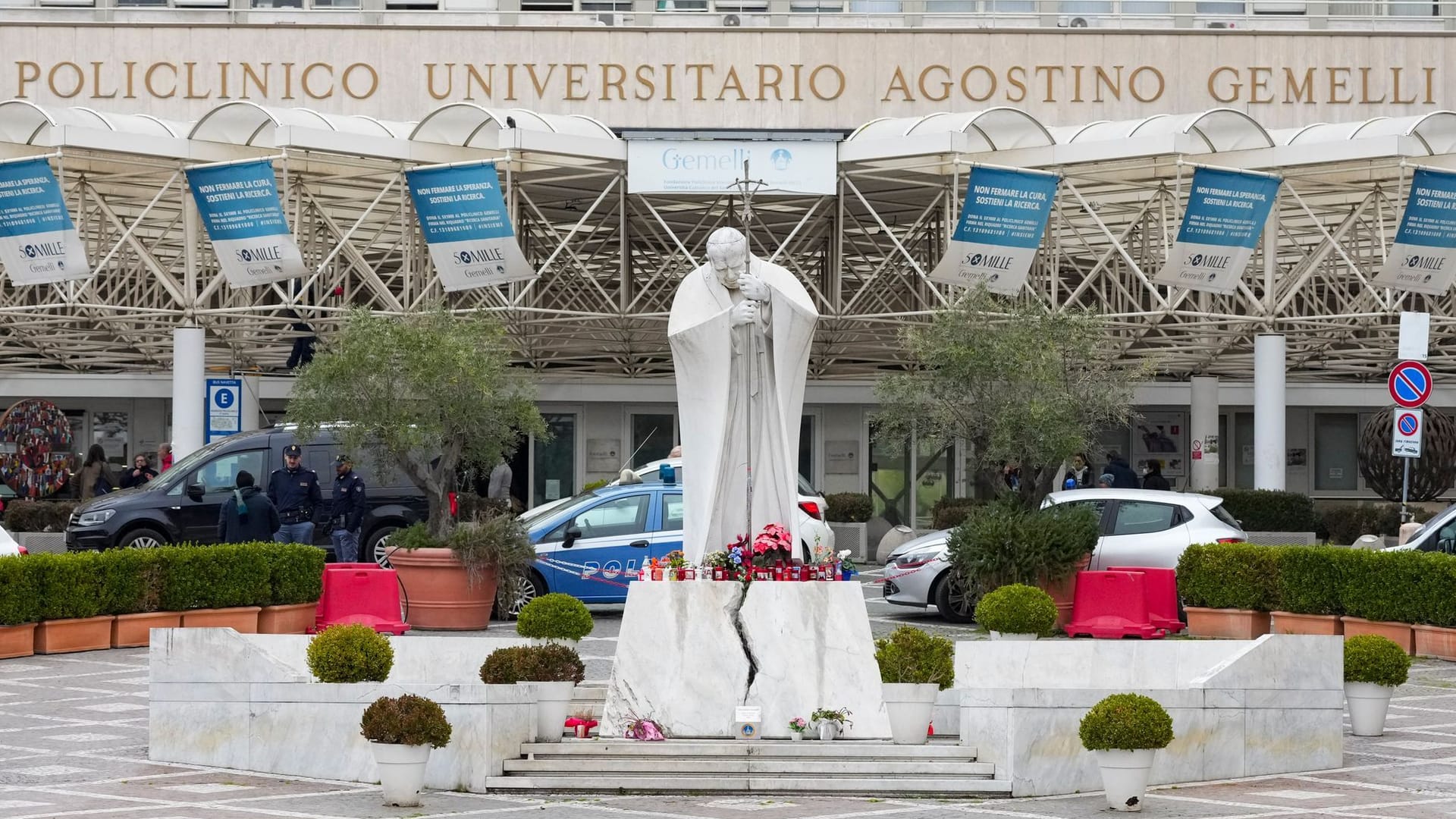 Eine Statue von Papst Johannes Paul II. vor der Poliklinik Agostino Gemelli in Rom: Gläubige haben Blumen und Kerzen aufgestellt.