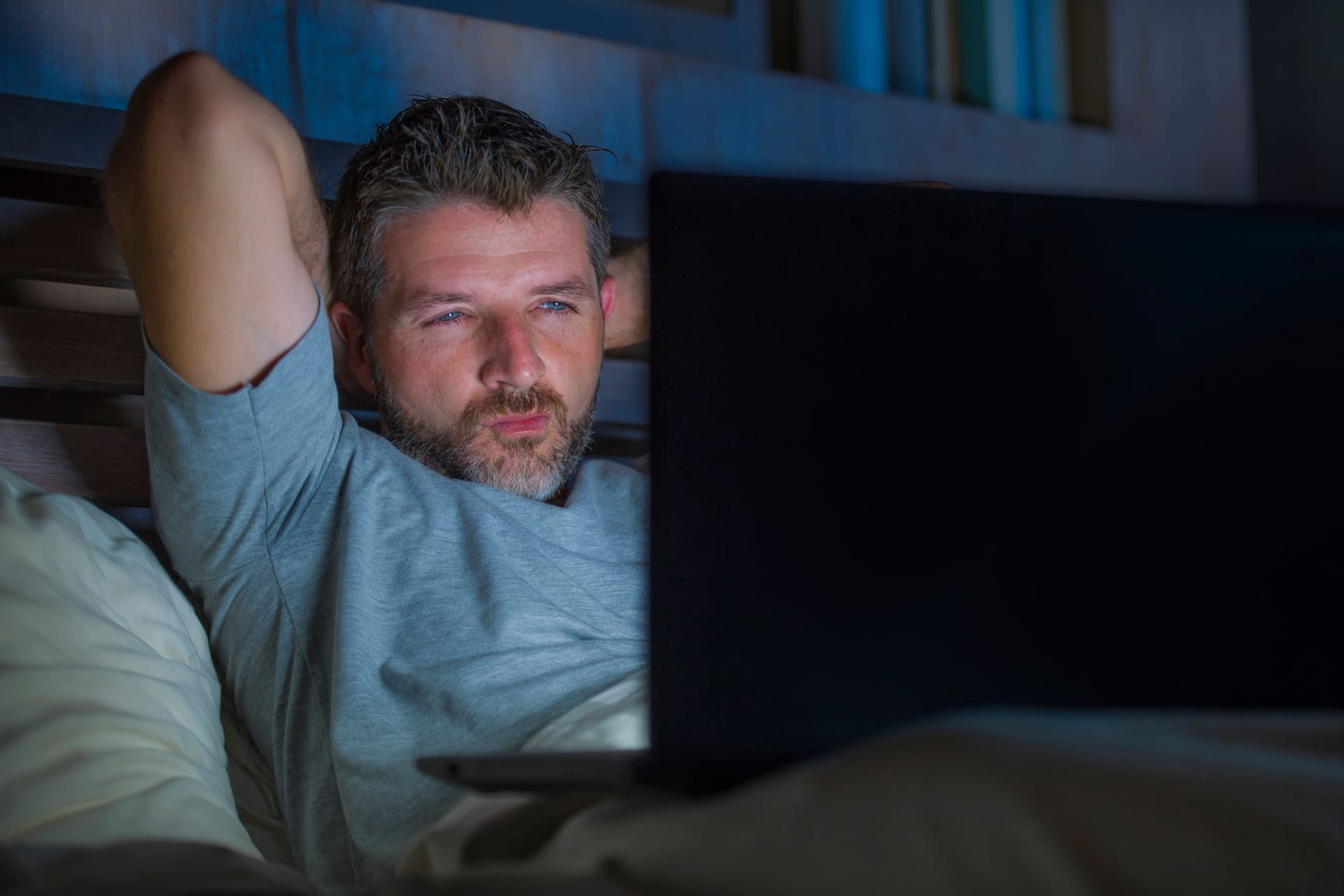 man alone in bed playing cybersex using laptop computer watching porn sex movie late at night with lascivious pervert face expression in internet pornographic sexual content