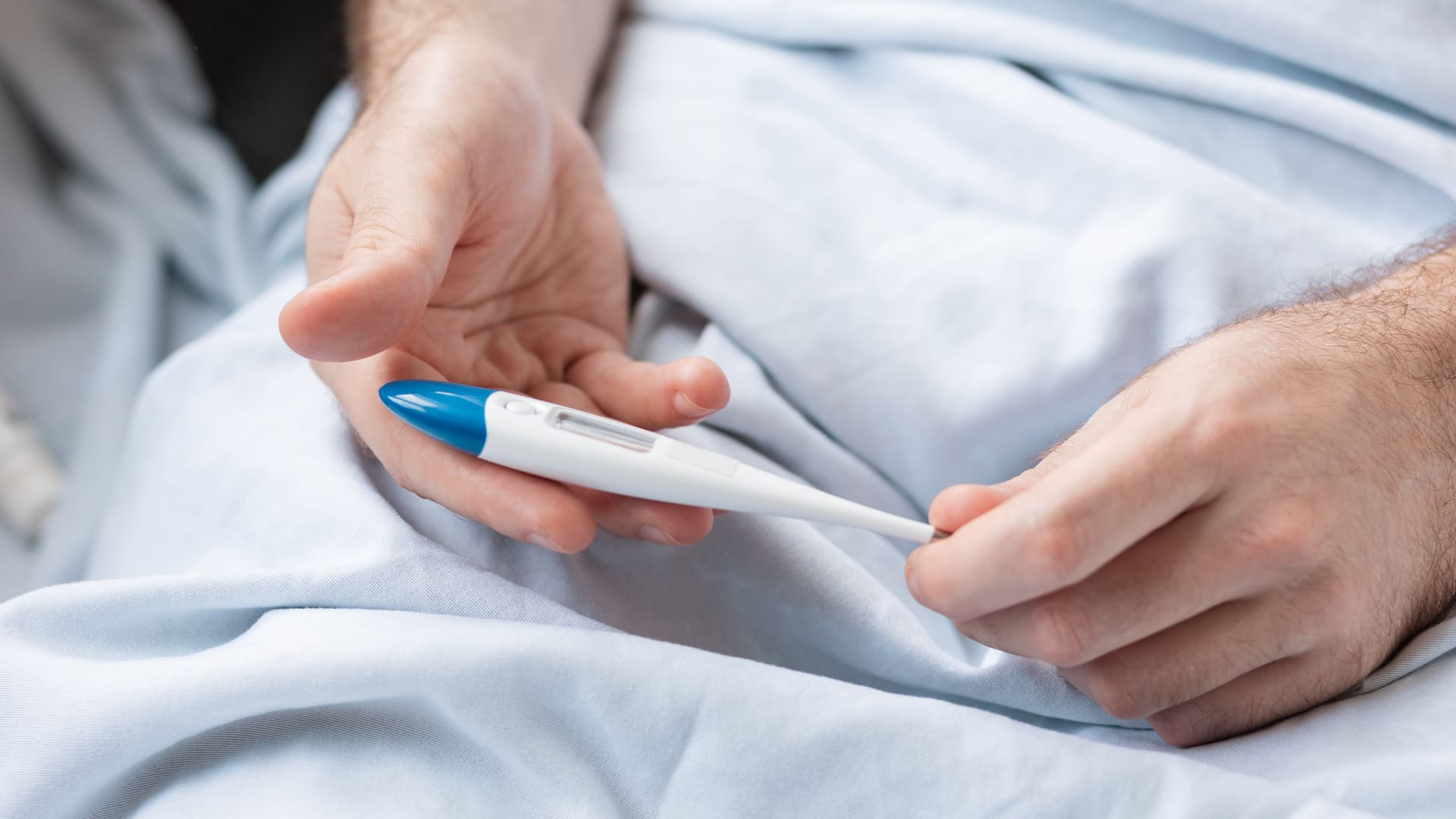 Mann hält Fieberthermometer in der Hand: 41 Grad Fieber und mehr sind für den Körper sehr belastend.