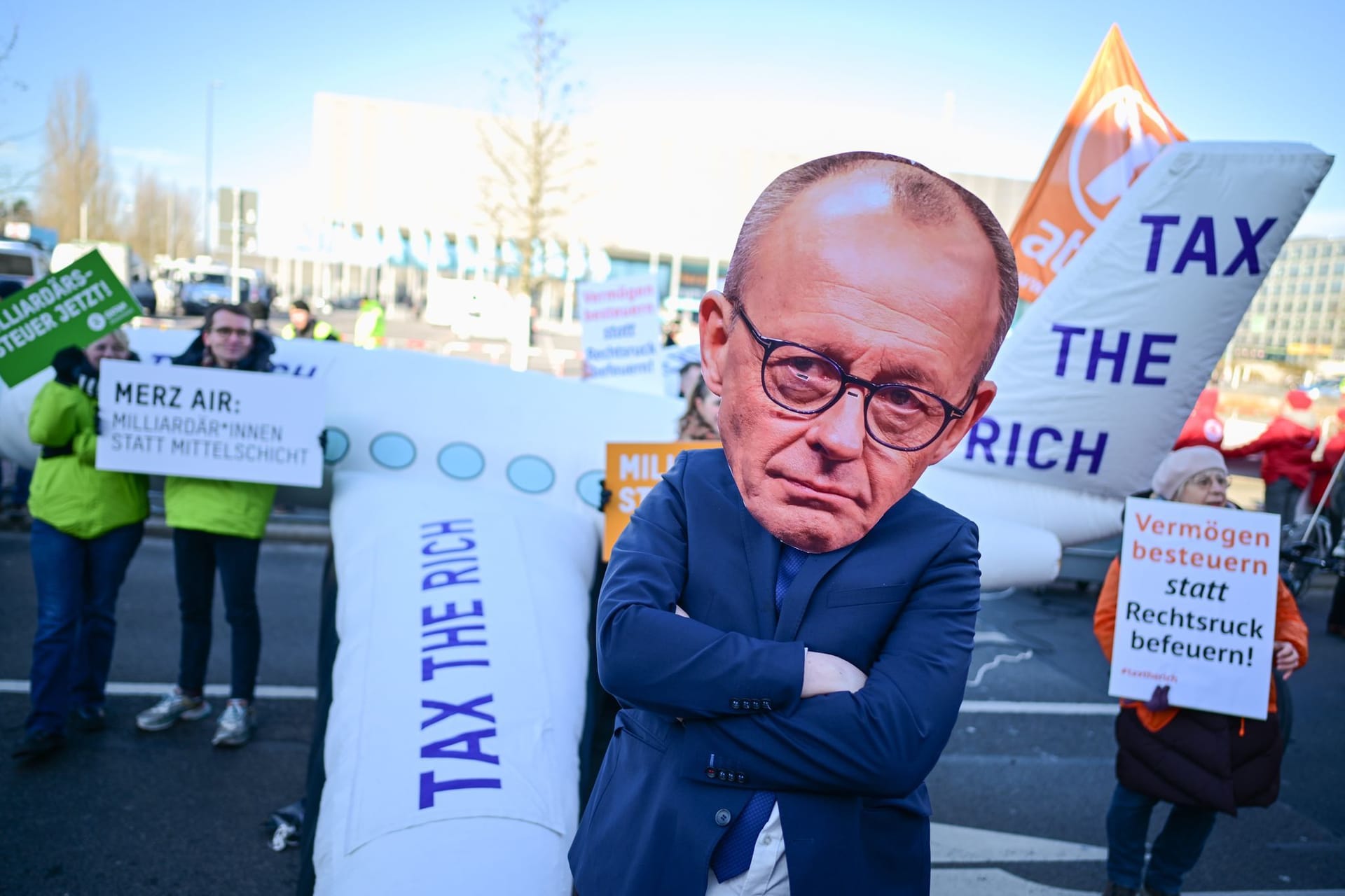Teilnehmer für eine Besteuerung von Vermögen stehen während einer Demonstration vor Beginn des 37. Bundesparteitag der CDU im CityCube Berlin vor dem Gelände.