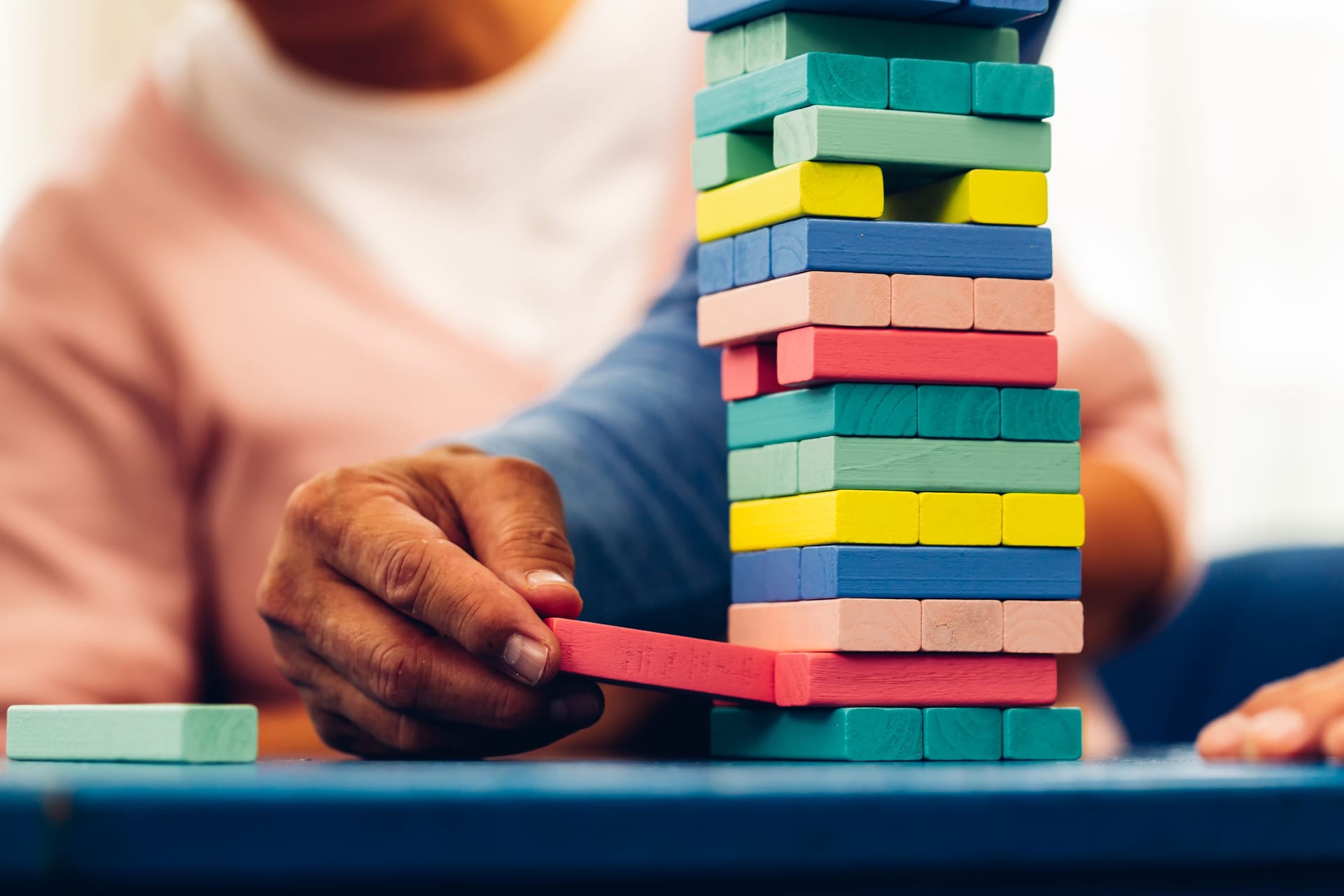 Senior people playing a wooden block tower, risk and strategy of project management. Concept of business risk with domino blocks. Older People playing jenga block removal game on table at home