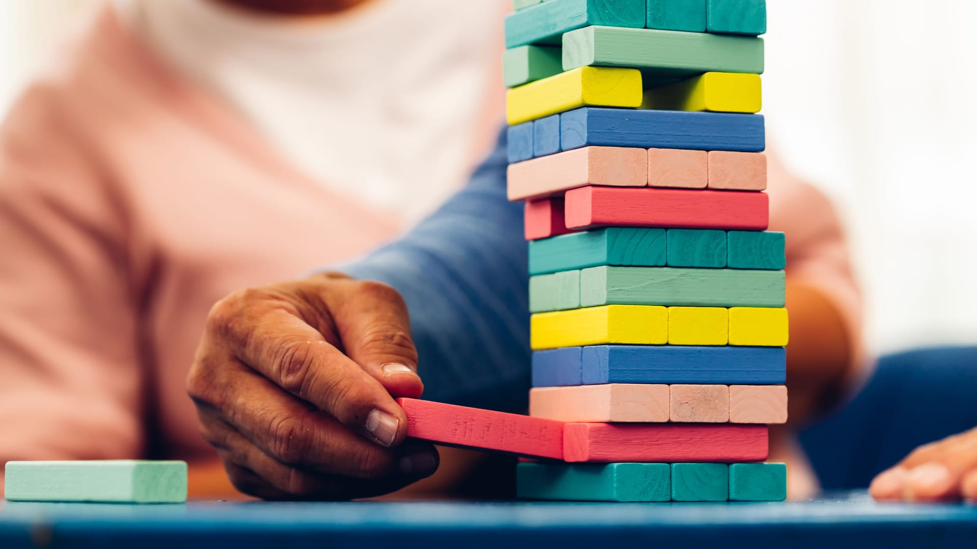 Senior people playing a wooden block tower, risk and strategy of project management. Concept of business risk with domino blocks. Older People playing jenga block removal game on table at home