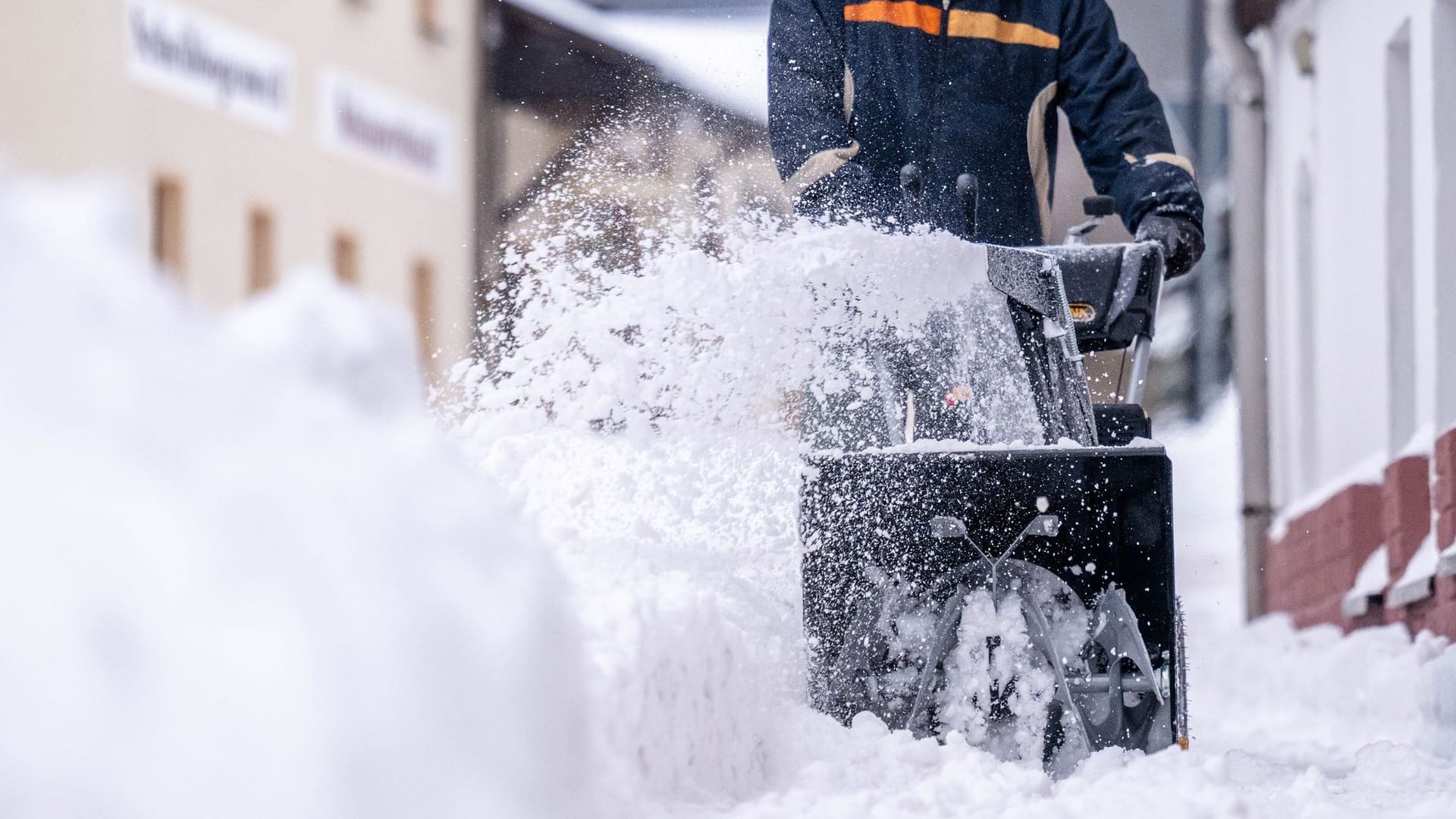 Ein Mann beräumt den Gehweg mit einer Schneefräse