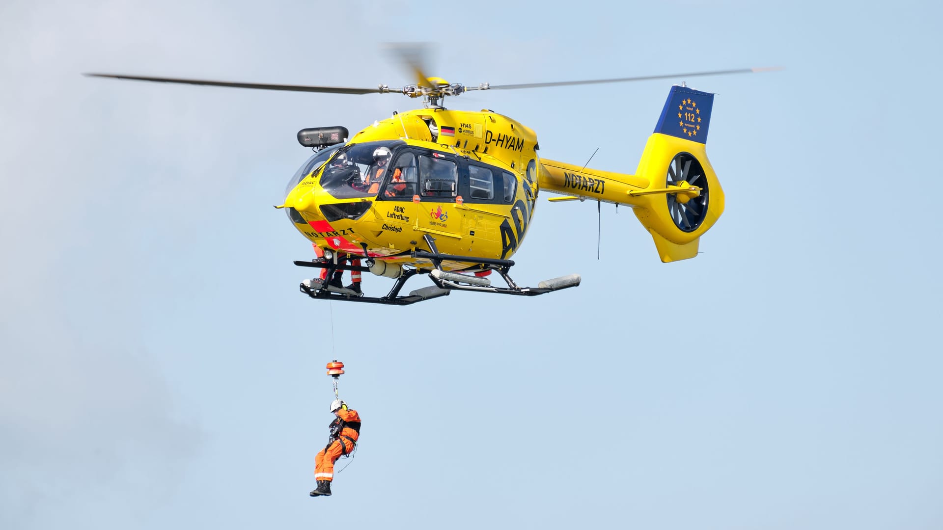 Person rappels down from a hovering ADAC rescue helicopter, in flight shot.