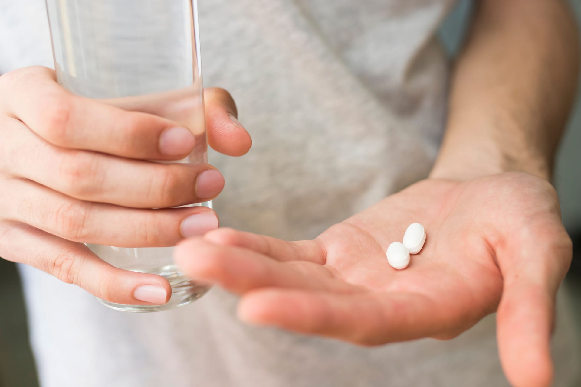 Jemand hält ein Glas Wasser in der einen und Tabletten in der anderen Hand: Die Einnahme von Ciprofloxacin kann vereinzelt Folgeschäden nach sich ziehen.