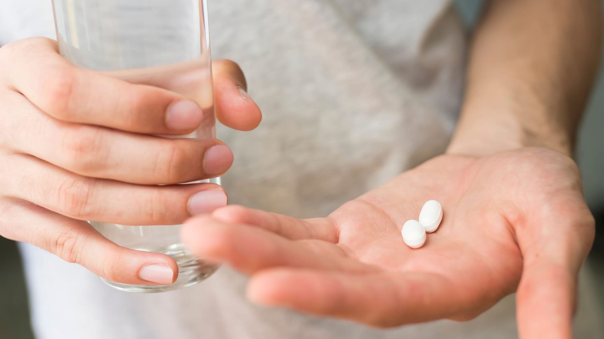 Jemand hält ein Glas Wasser in der einen und Tabletten in der anderen Hand: Die Einnahme von Ciprofloxacin kann vereinzelt Folgeschäden nach sich ziehen.