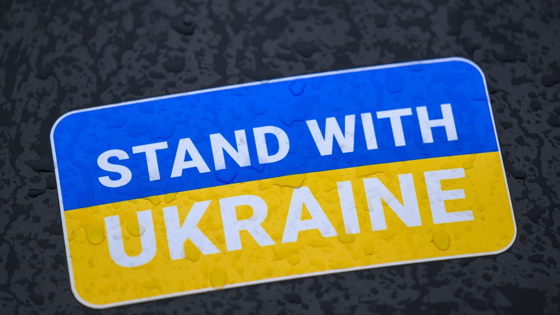 "Stand with Ukraine" steht auf einem Aufkleber in den Landesfarben der Ukraine.