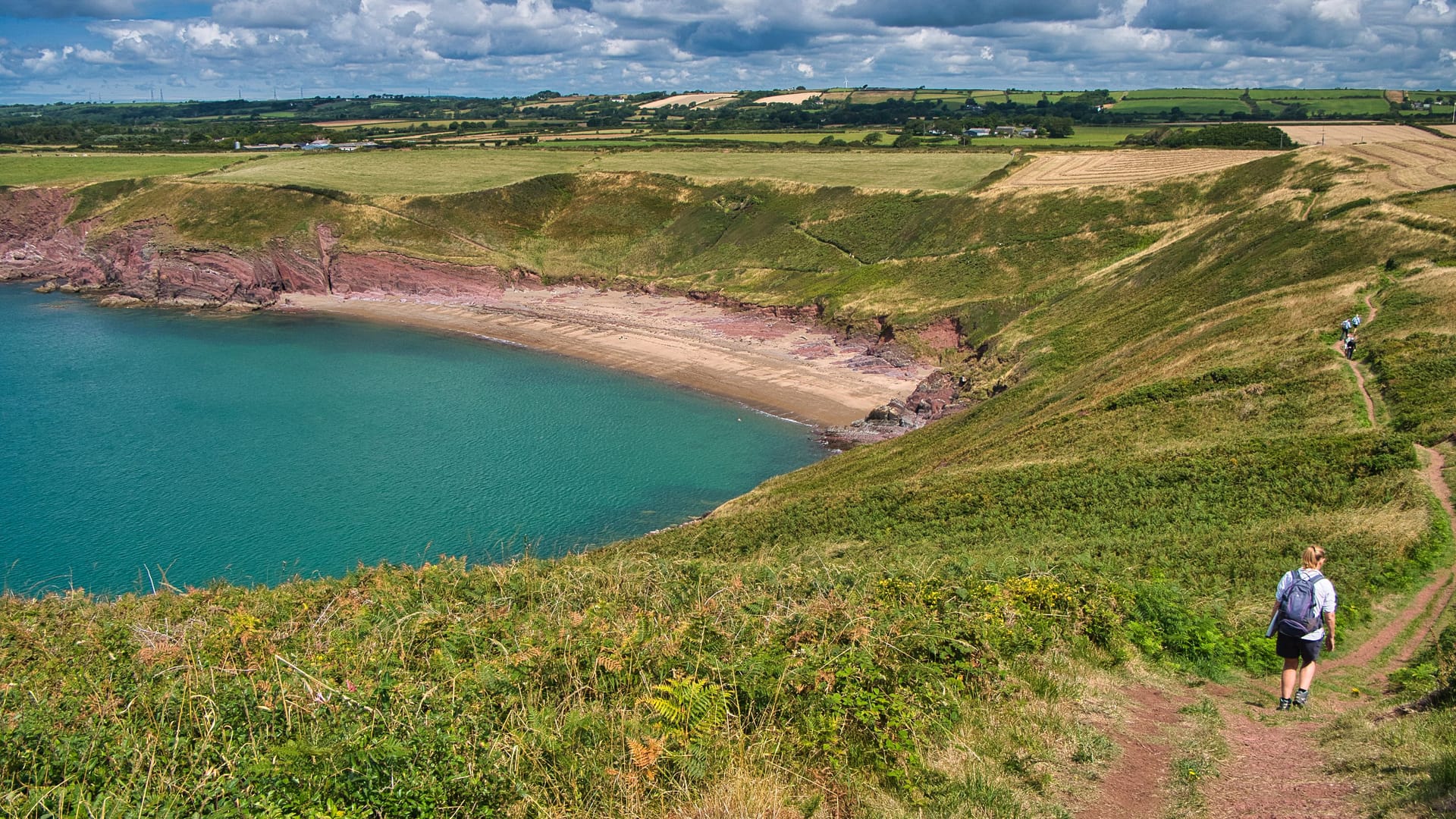 Ein Wanderer läuft über den roten Sandweg am Swanlake Beach: Der Pembrokeshire Coast Path gehört bei vielen Wanderern auf die Bucket-Liste.