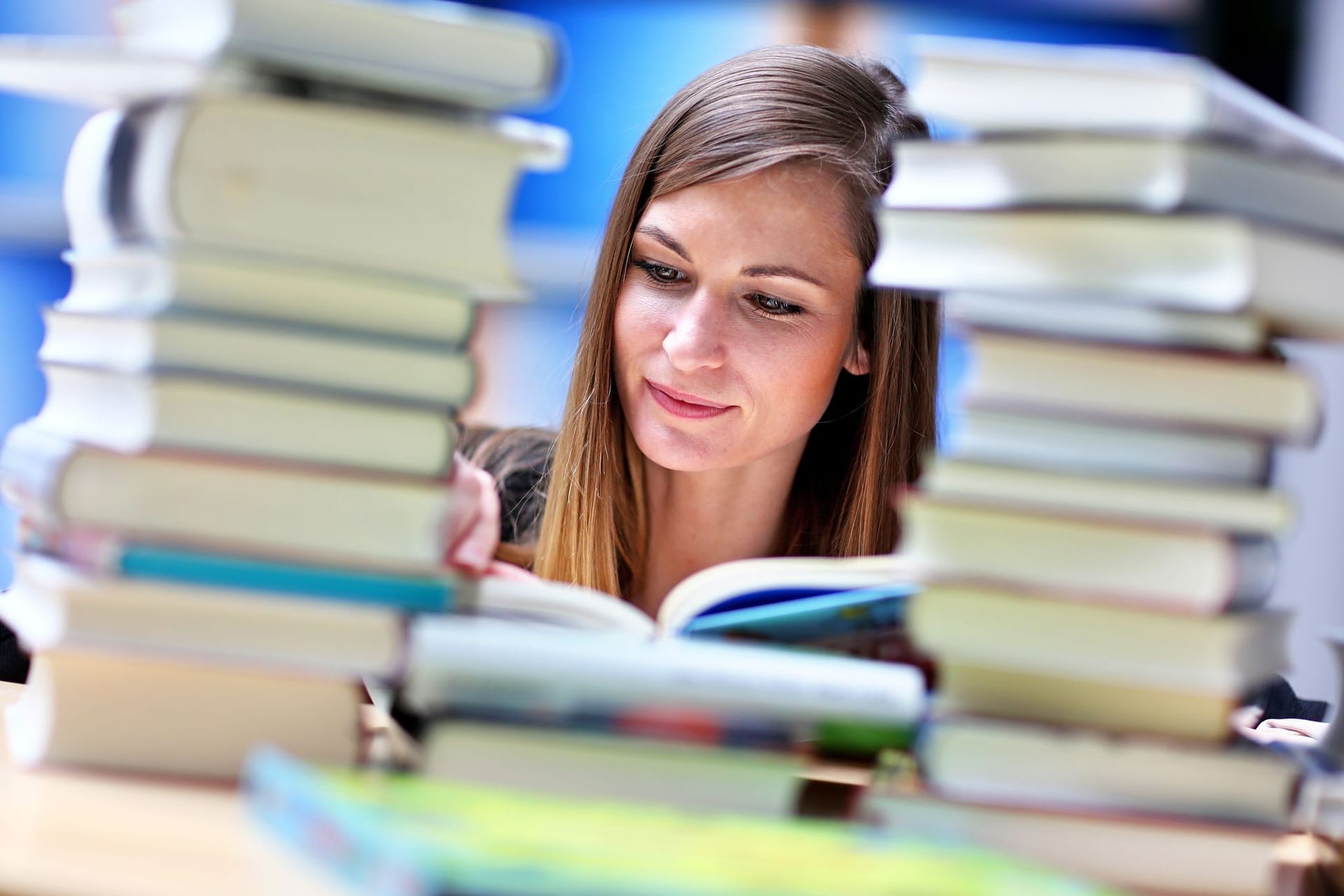 Frau liest an einem Tisch voller Bücher