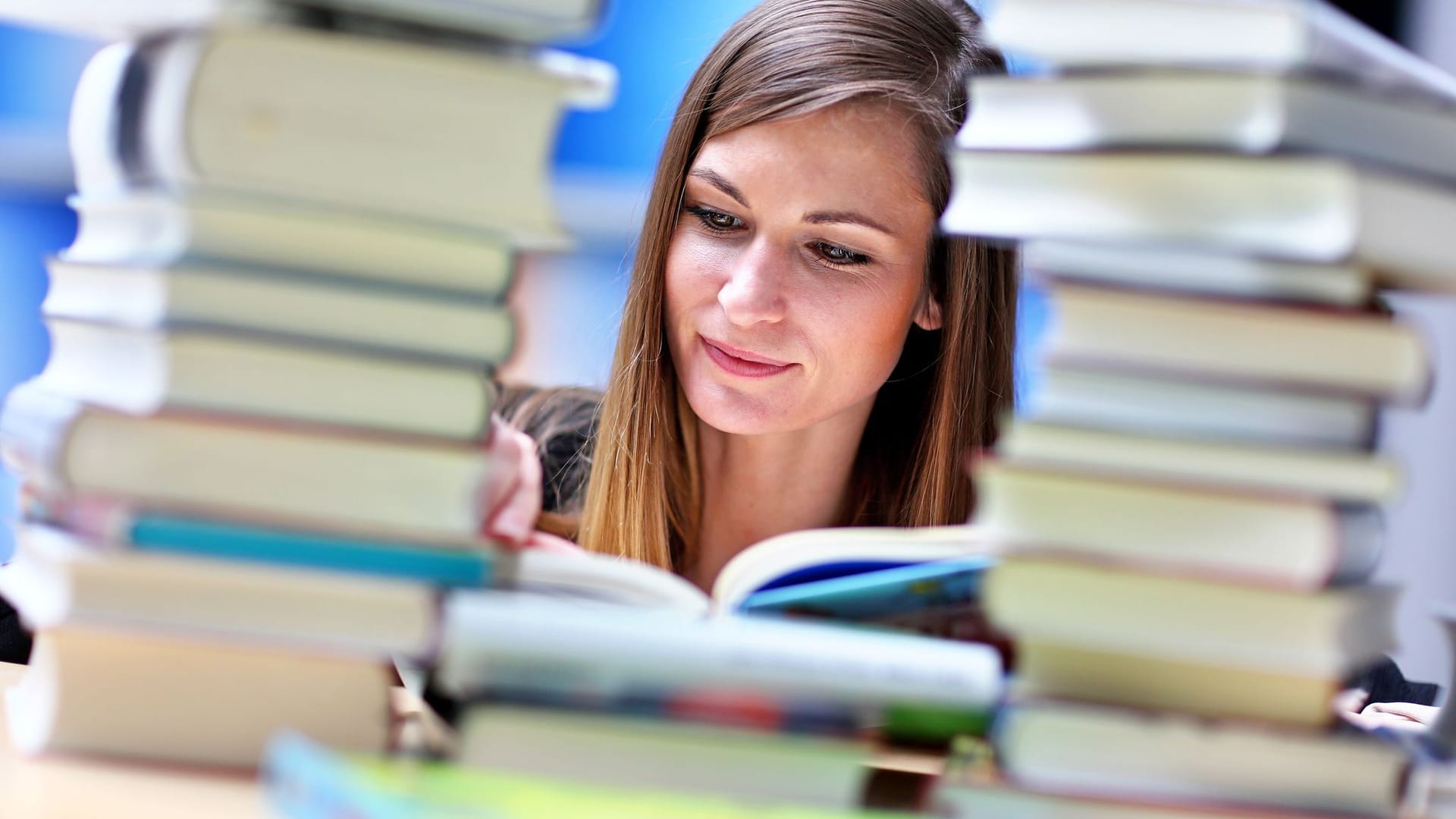 Frau liest an einem Tisch voller Bücher