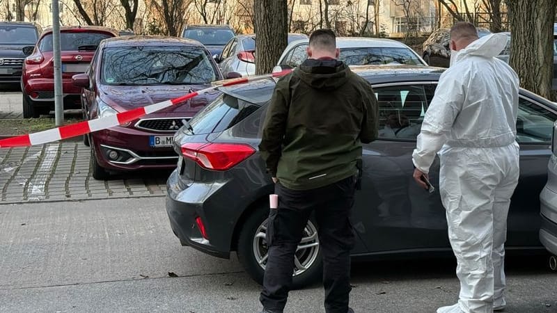 Zwei Beamte der Spurensicherung stehen vor einem Auto, das mit Absperrband gesichert ist: Ein Mann ist nach einer Gewalttat in Marzahn gestorben.