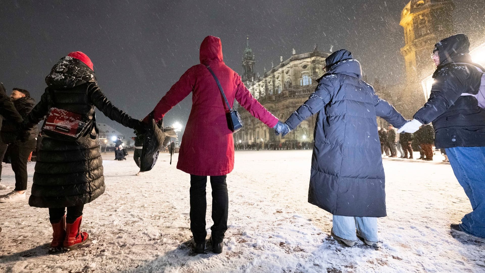 13.02.2025, Sachsen, Dresden: Passanten stehen am 80. Jahrestag der Zerstörung Dresdens bei einer Menschenkette auf dem Theaterplatz vor der Katholischen Hofkirche. Am 13. Februar gedenkt die Landeshauptstadt Dresden der Zerstörung der Stadt im Zweiten Weltkrieg vor 80 Jahren. Am 13. und 14. Februar 1945 legten alliierte Bomber das Zentrum der Elbestadt in Schutt und Asche. Bis zu 25.000 Menschen kamen dabei ums Leben. Foto: Sebastian Kahnert/dpa